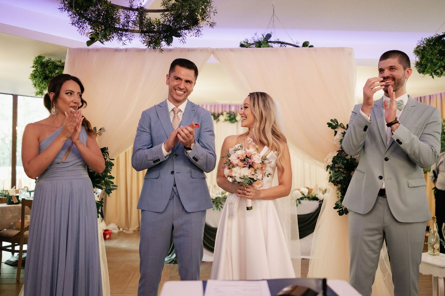 Wedding party members in gray and white attire celebrate during a ceremony in an indoor venue.