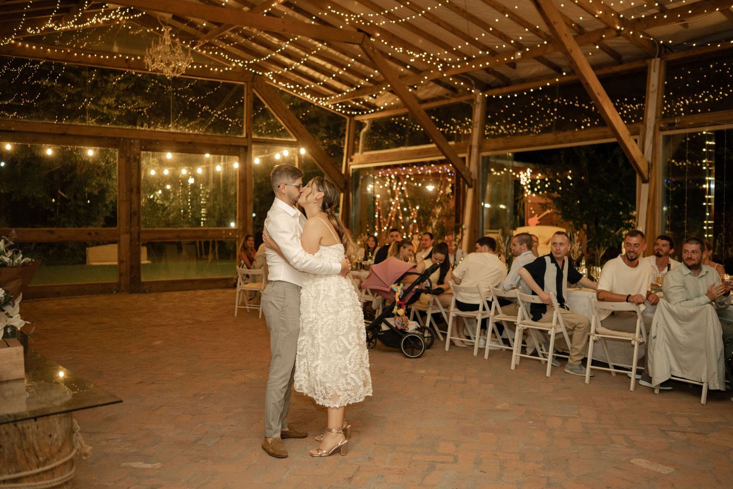Wedding reception dance floor illuminated by string lights in rustic barn venue during evening celebration.