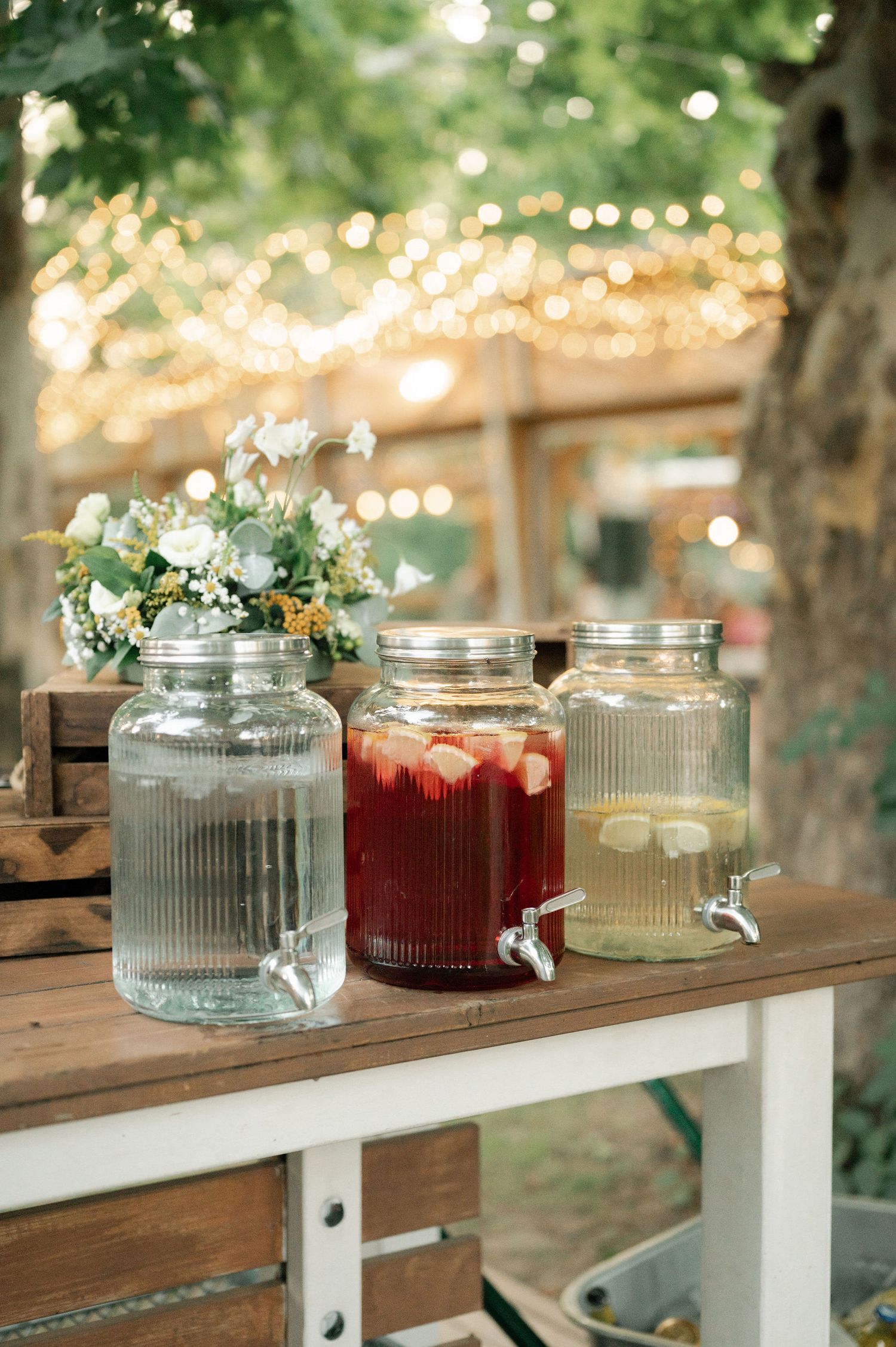 Glass jars with flowers arranged on a rustic wooden shelf with twinkle lights creating a romantic outdoor setting.