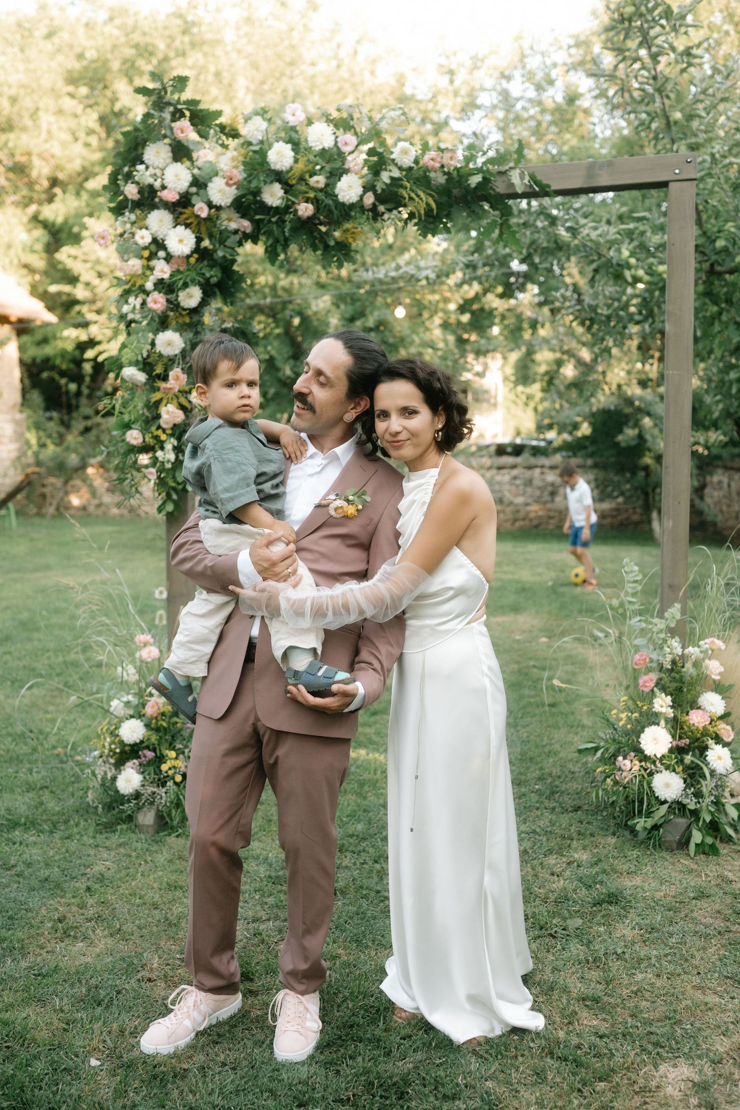 A playful wedding moment captured in a garden setting with white roses climbing on wooden posts.