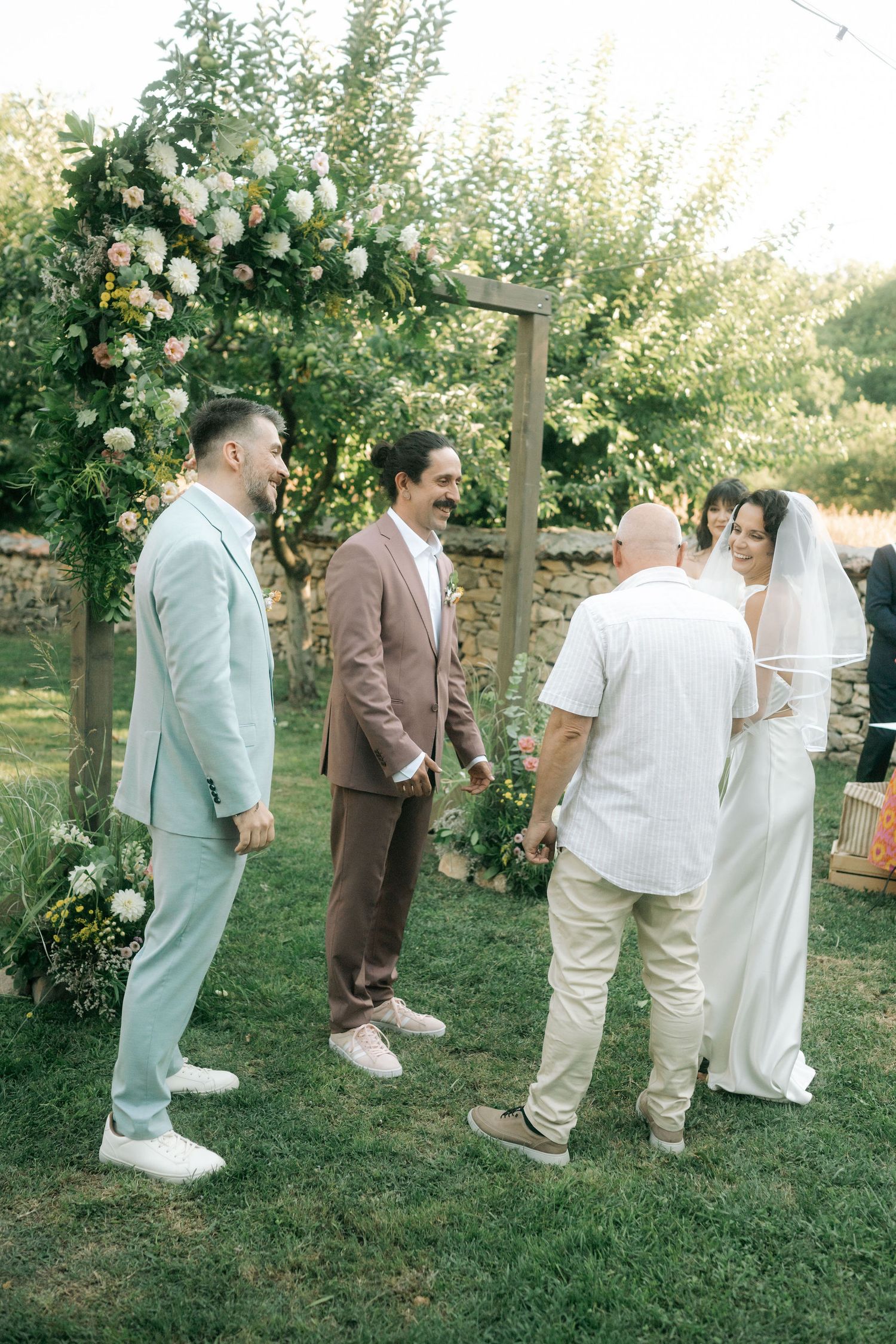 A wedding party poses together on a grassy lawn with blooming rose bushes in the background.