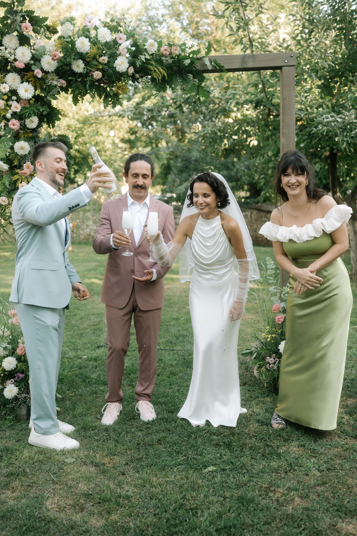 Wedding party members in white and sage green dresses pose playfully on grass in a candid photo series.