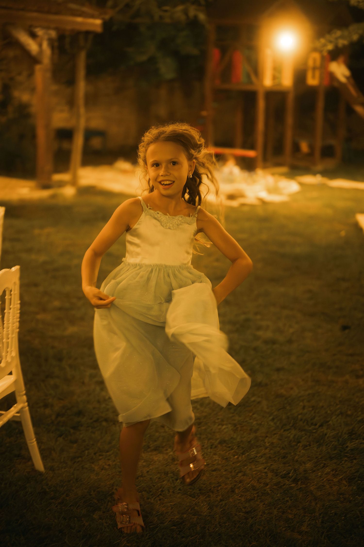 A series of four connected photos showing a child in a white dress playing and dancing in a dimly lit outdoor setting at dusk.