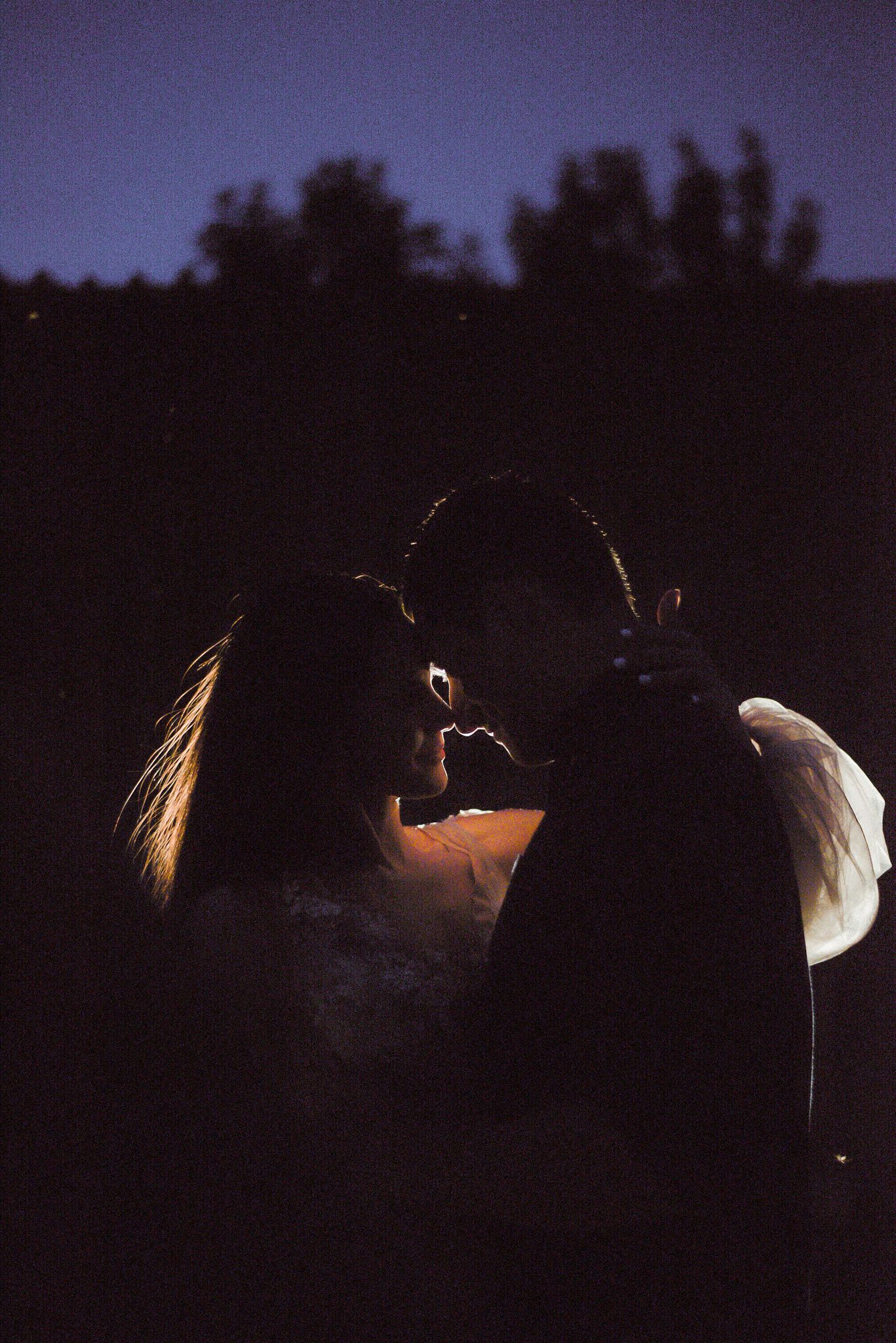 A silhouetted couple sharing an intimate moment at dusk with a soft glow illuminating their profiles.