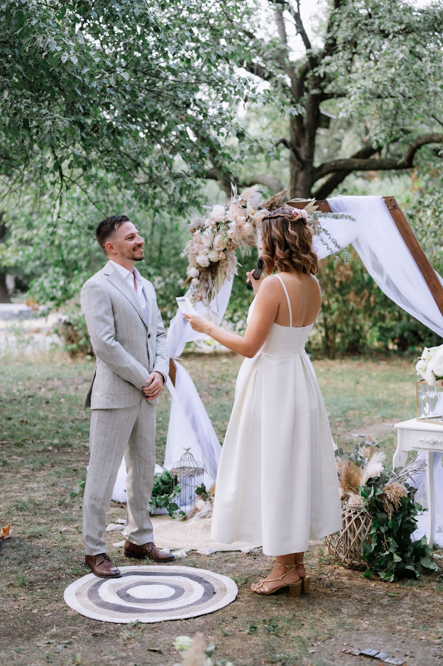 Romantic outdoor wedding ceremony under olive trees with white decor and floral arrangements.