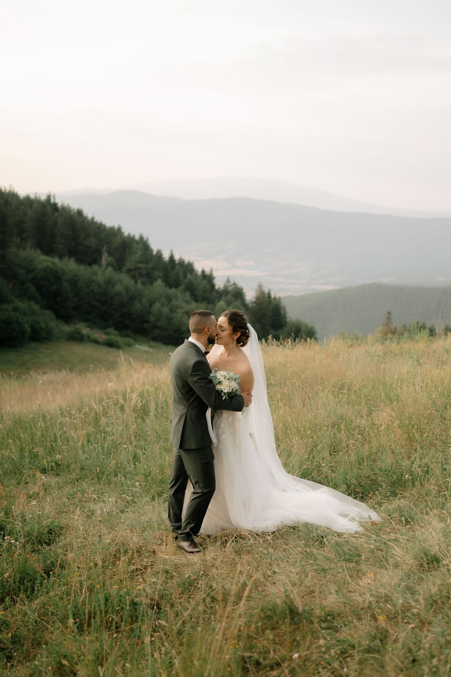 A couple shares an intimate moment in a scenic mountain meadow during their outdoor wedding ceremony.