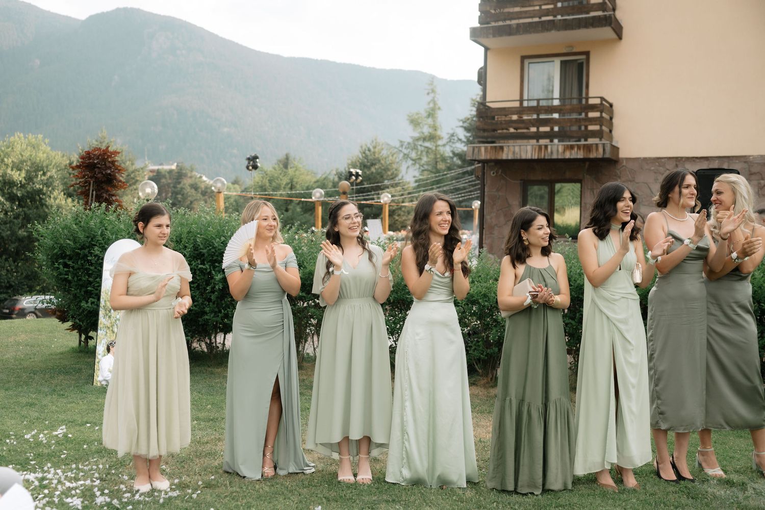 Wedding party wearing sage green and neutral dresses stand together in front of mountain scenery.
