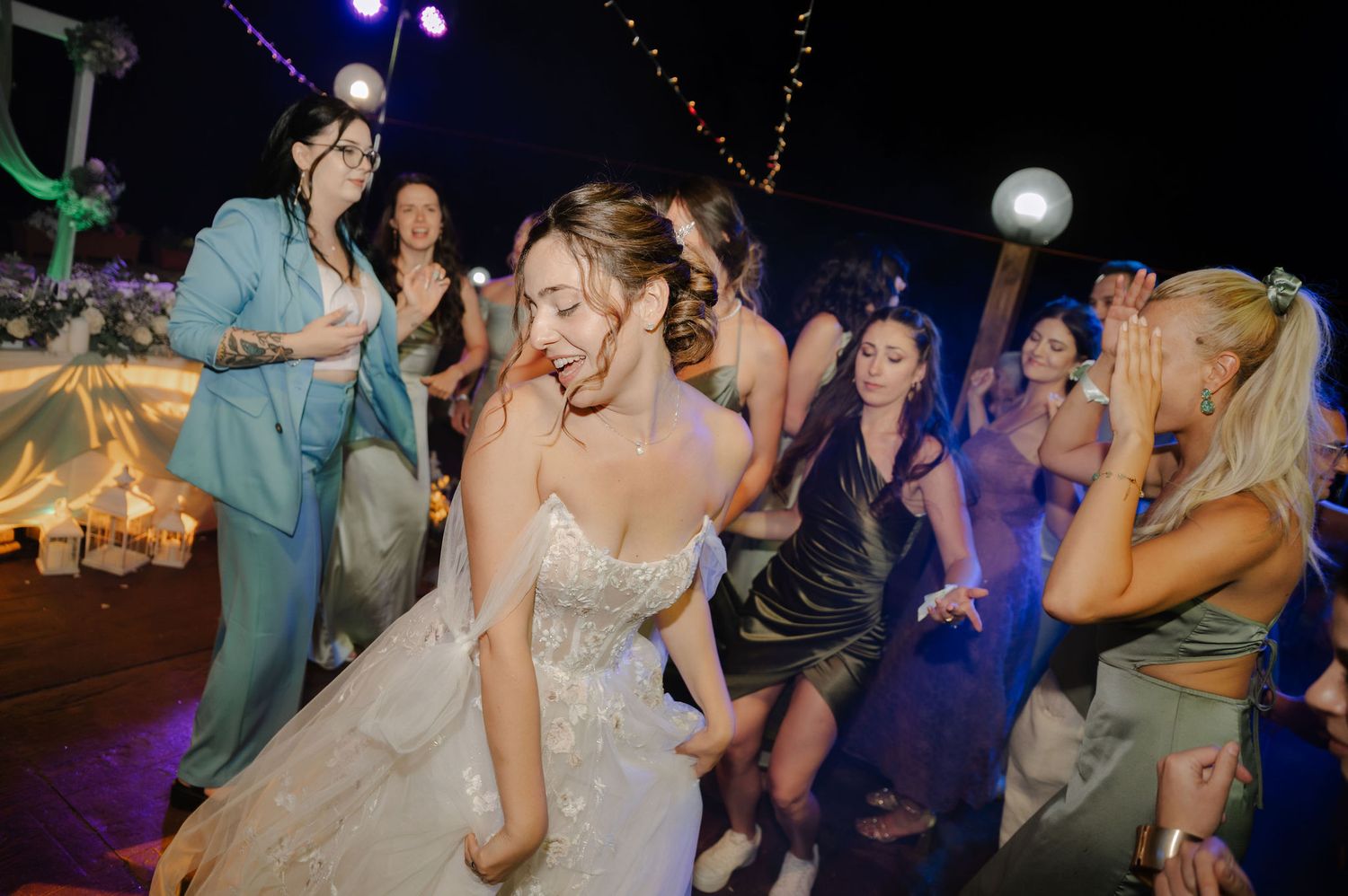 People dancing and celebrating at a wedding reception with colorful lighting and festive atmosphere.