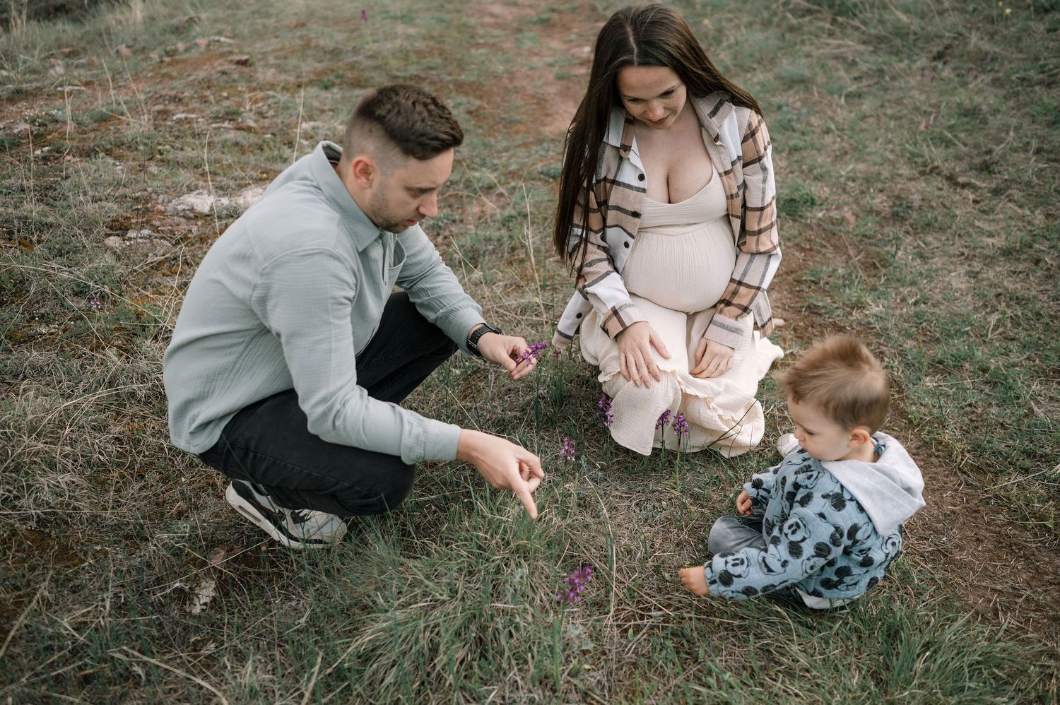A couple sits together on grass during an outdoor photo session showing affectionate moments.