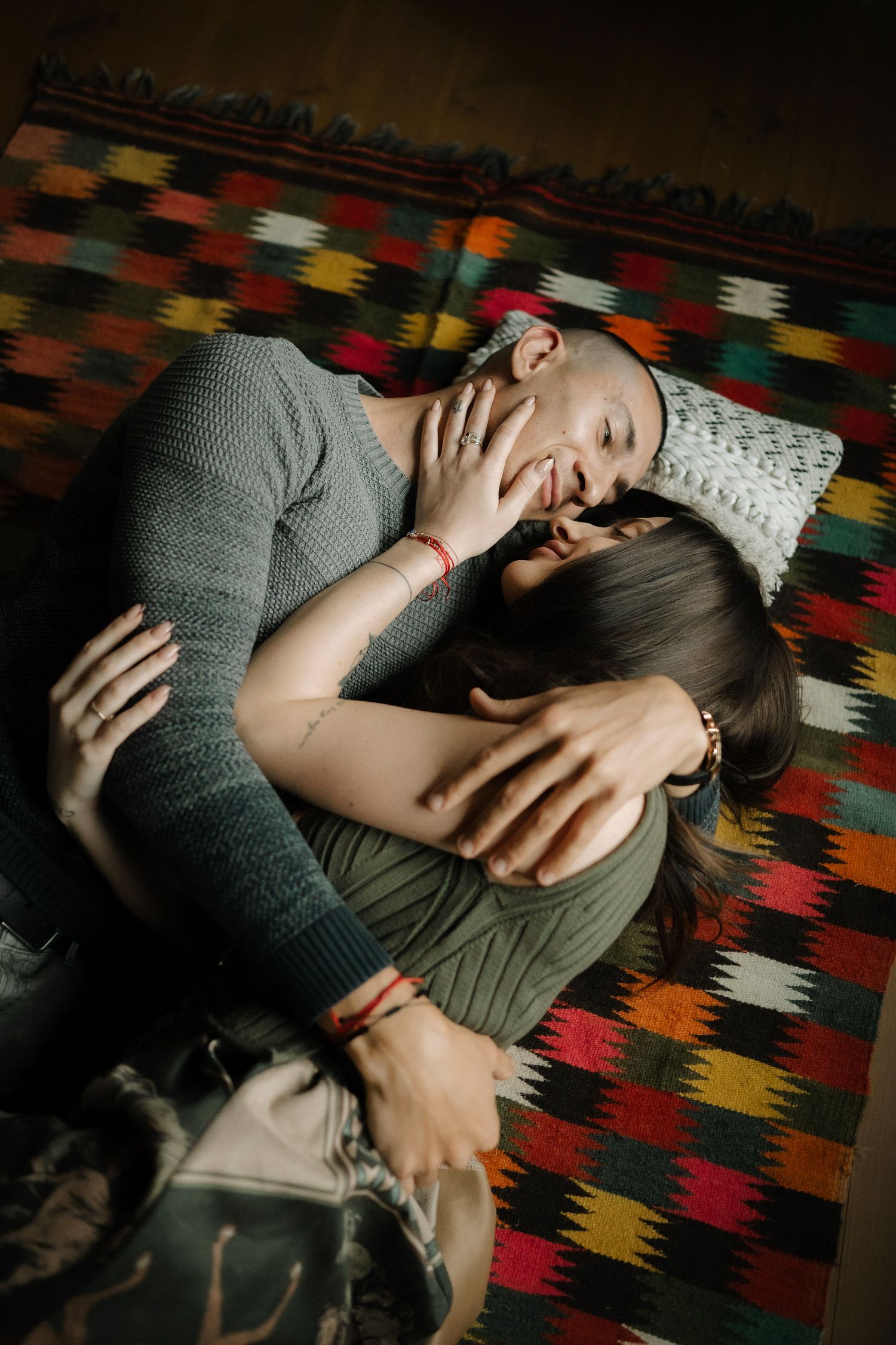 Person relaxing on vibrant geometric patterned carpet wearing gray sweater in dim lighting.