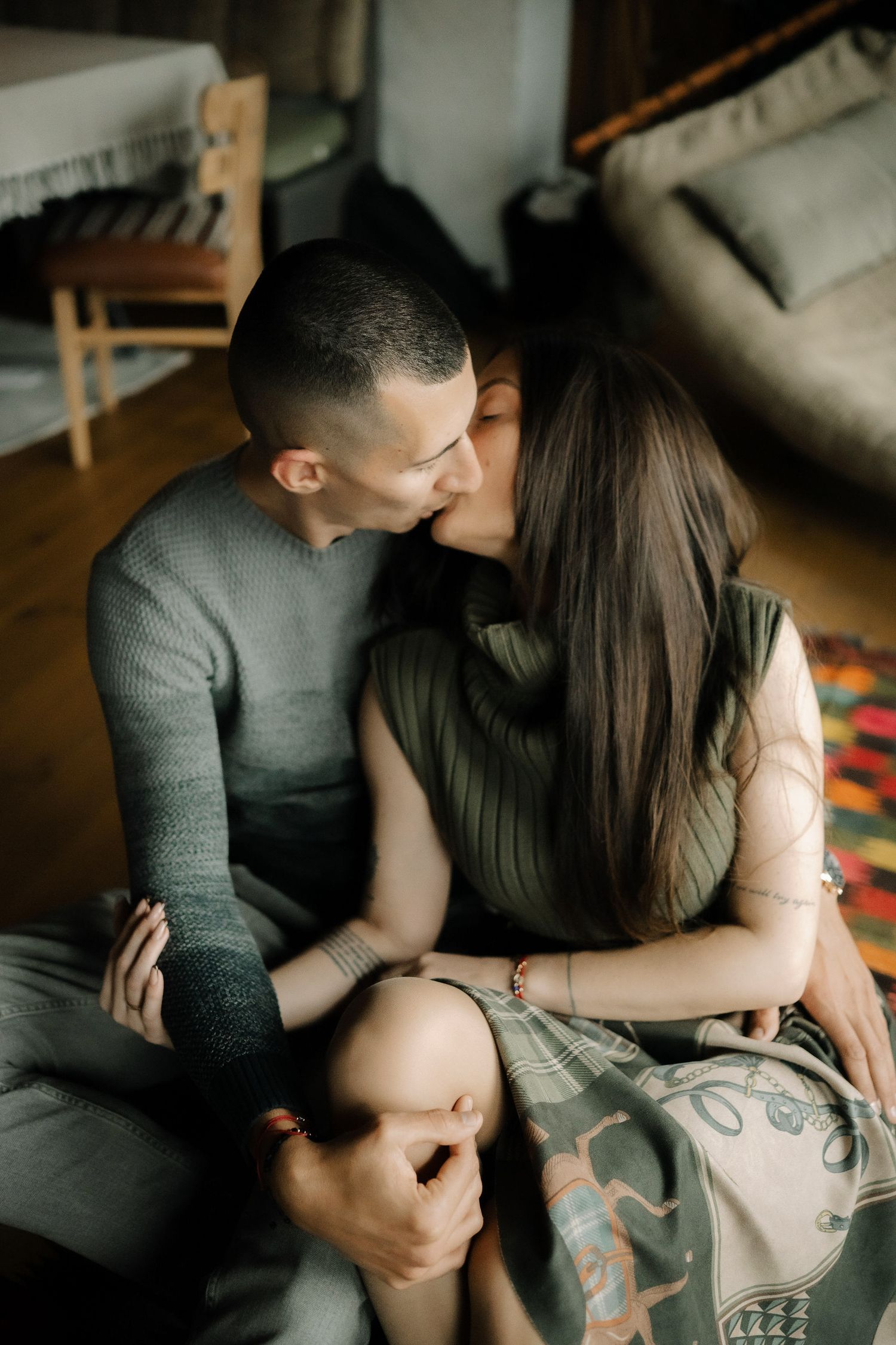Romantic couple embracing in moody lighting while showing colorful arm tattoos.
