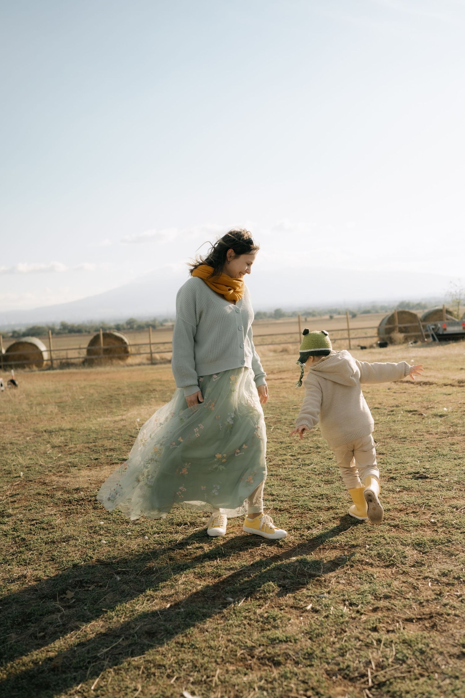 Two figures in light colored clothing cast long shadows while running and playing in an open field at sunset.