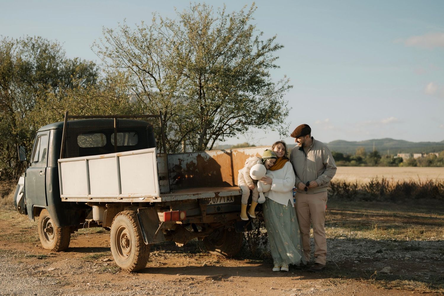 A couple embraces next to an old utility truck against a scenic rural landscape backdrop.