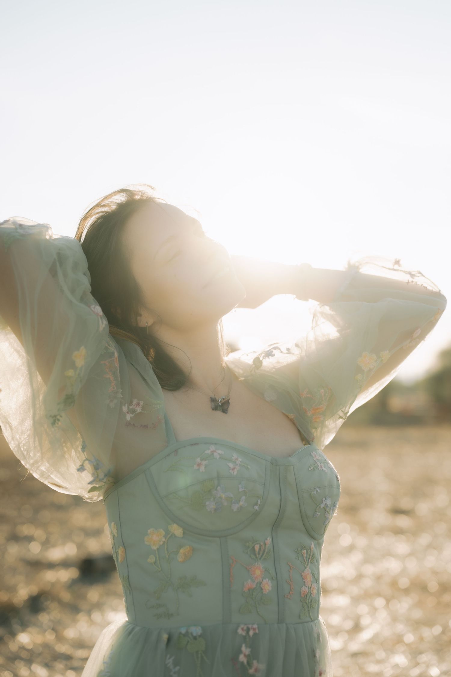A person in a flowy mint green dress with butterflies dances in golden sunlight during sunset.