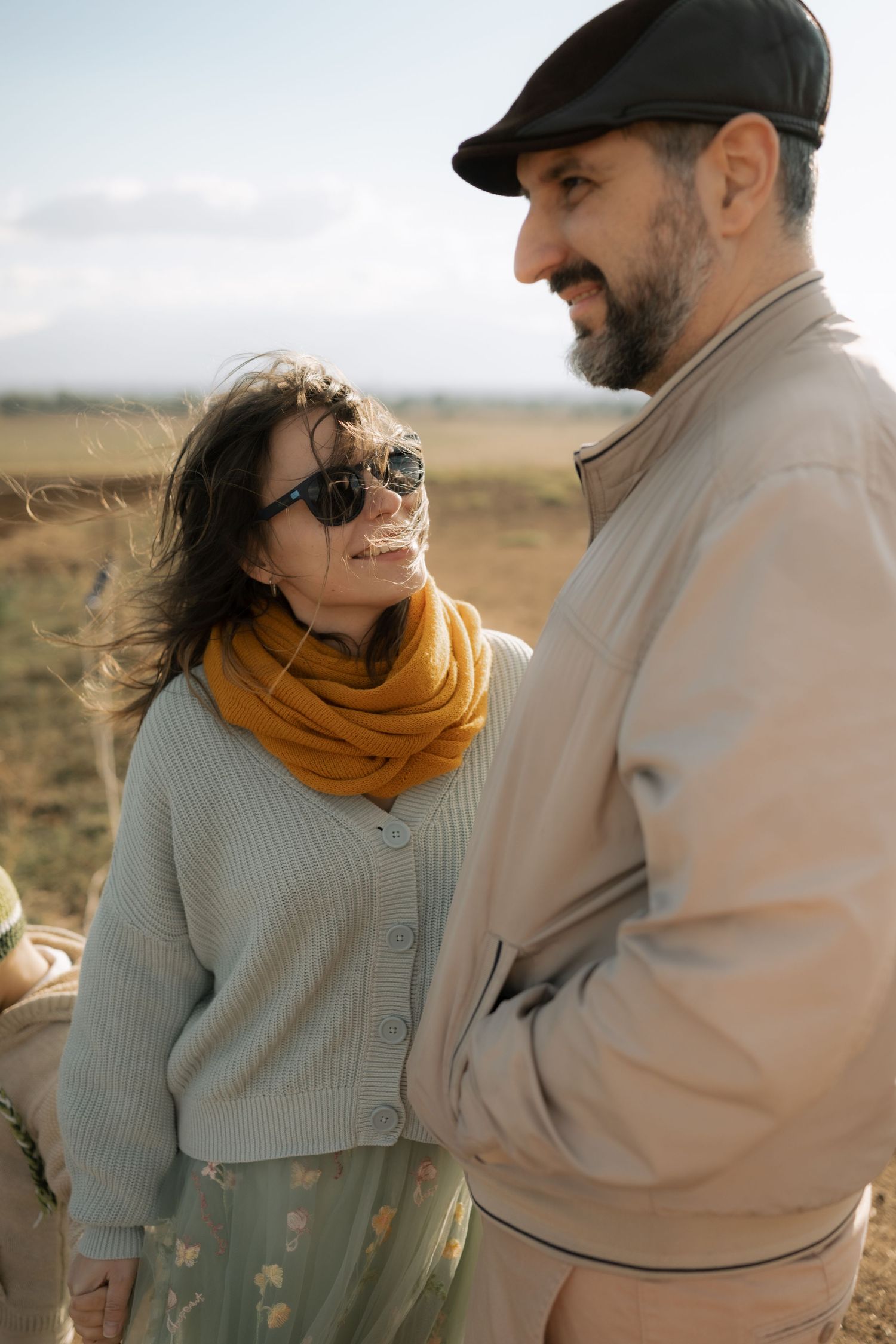 Couple in casual autumn attire sharing an intimate moment against a scenic outdoor landscape at sunset.