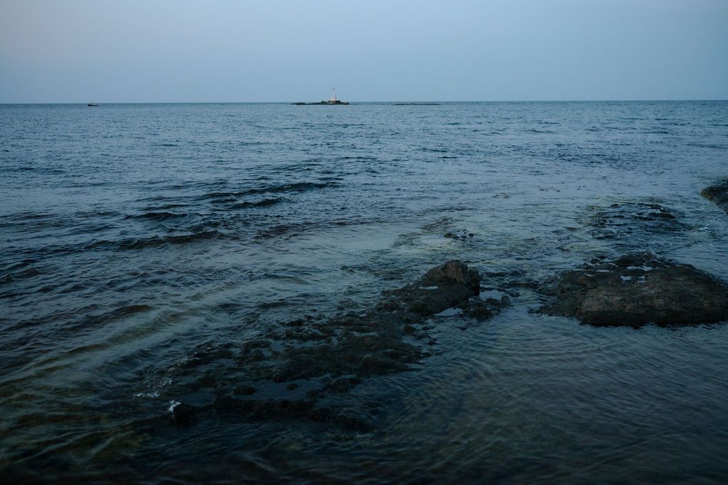 Dark moody seascape with rocky outcrops visible beneath the surface of deep blue ocean waters at dusk.