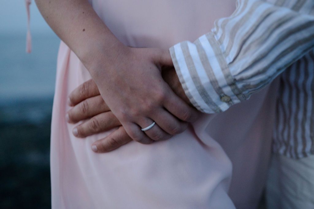 A couple holds hands in a romantic outdoor setting showing their engagement rings and matching striped sleeves.