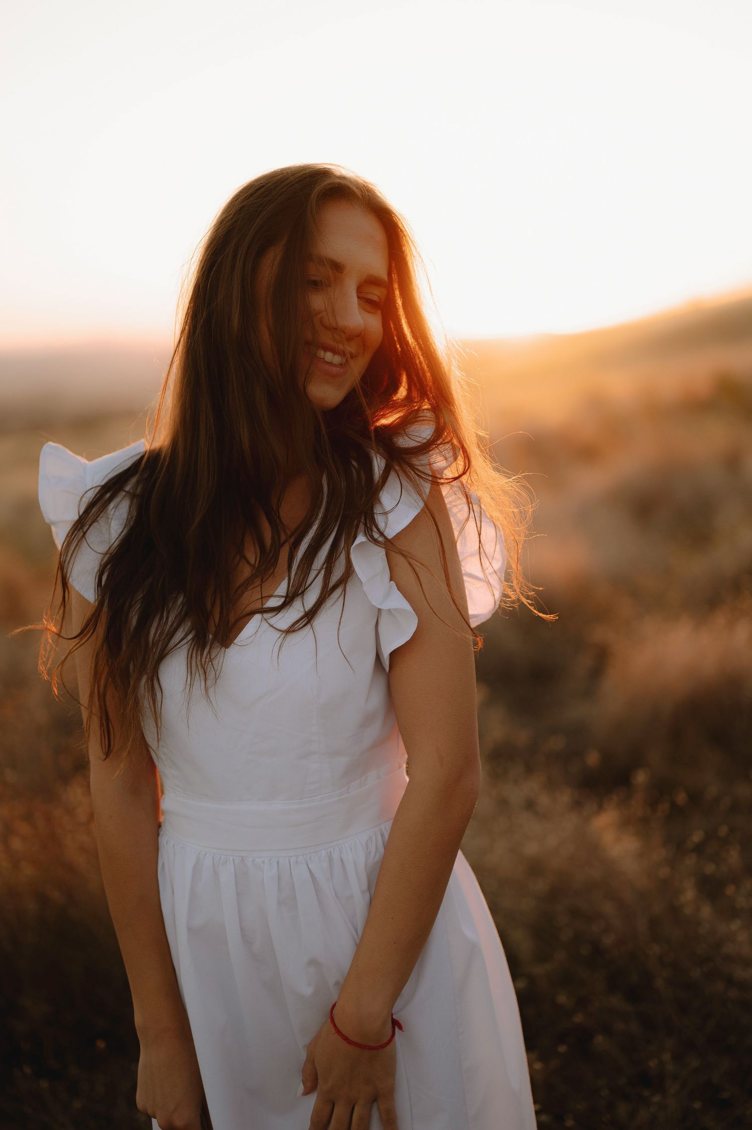 A person in a white dress stands in a desert landscape at golden hour as sunlight creates a dreamy atmosphere.