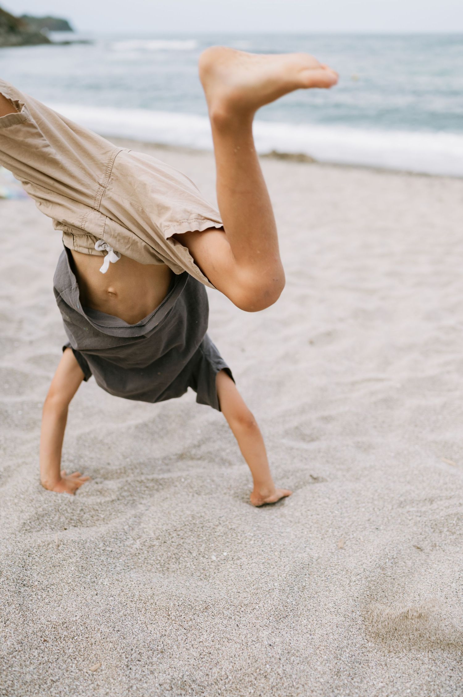 Child doing a cartwheel on a sandy beach with ocean waves in the background.