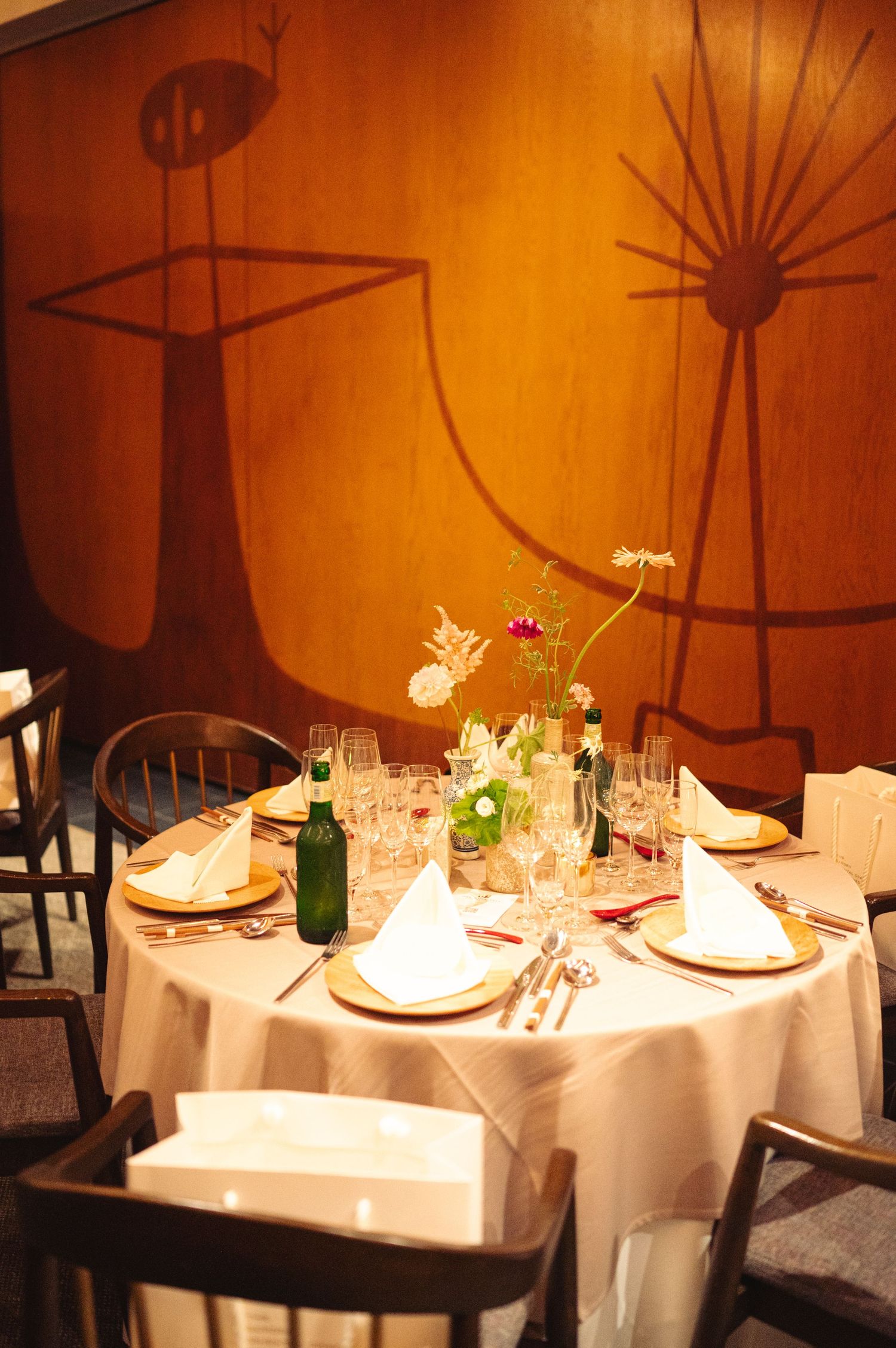 Dining tables with white linens set against warm orange walls with artistic silhouettes.
