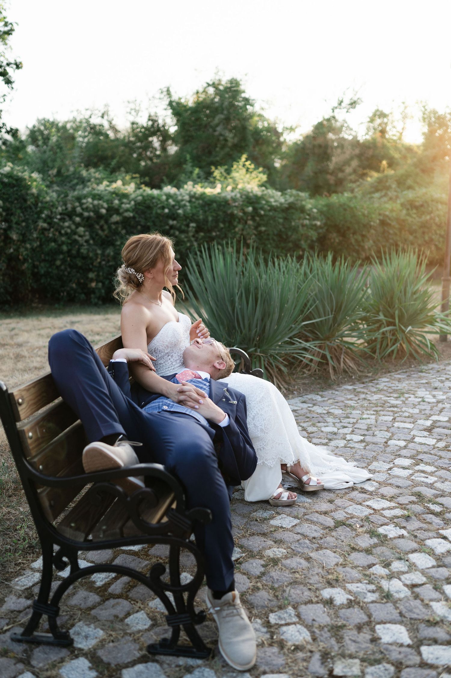 Sunset wedding photos of couple sharing intimate moments on park bench with garden backdrop.