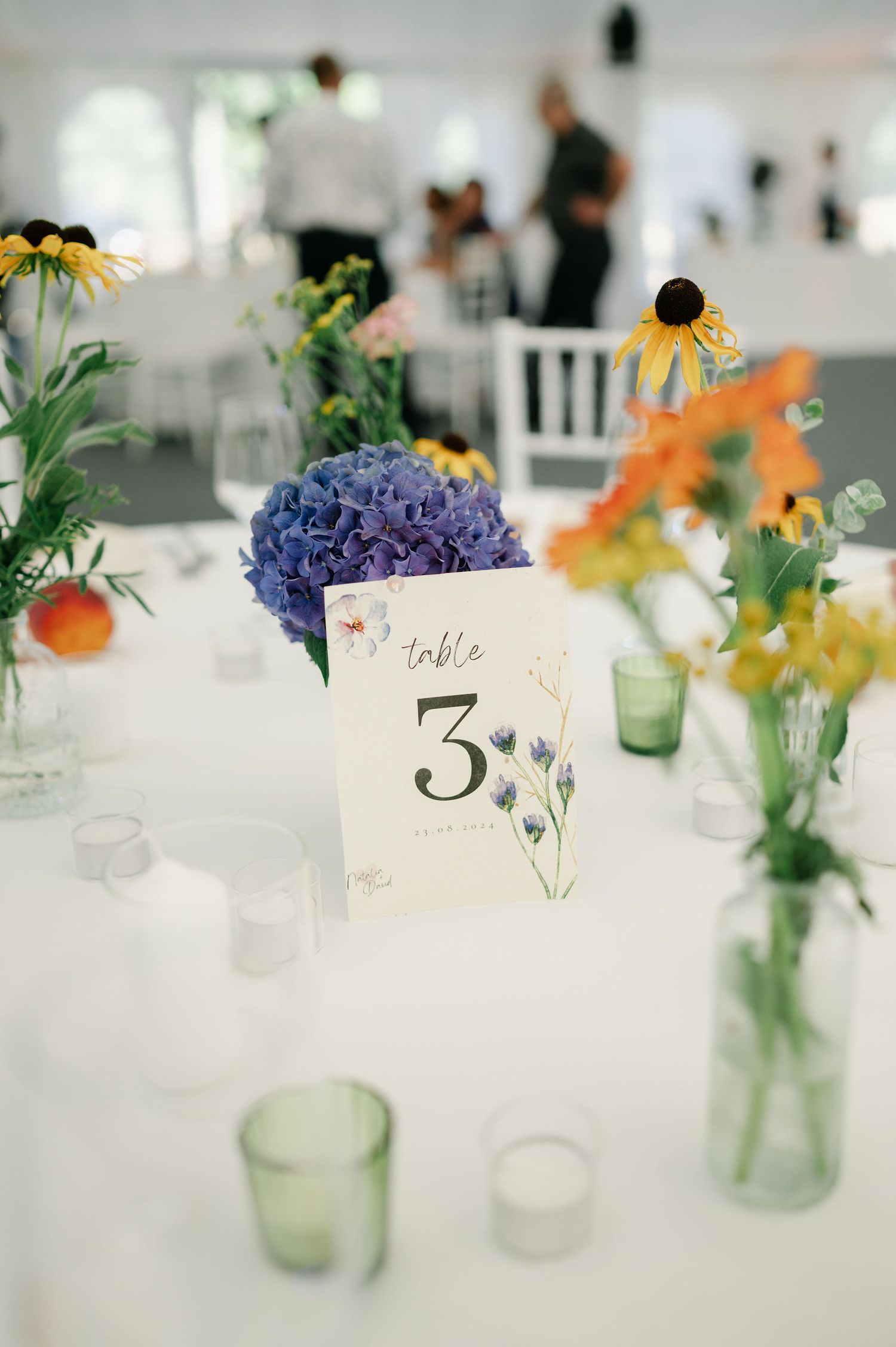 Wedding reception table with handpainted number cards and mason jar flower arrangements.