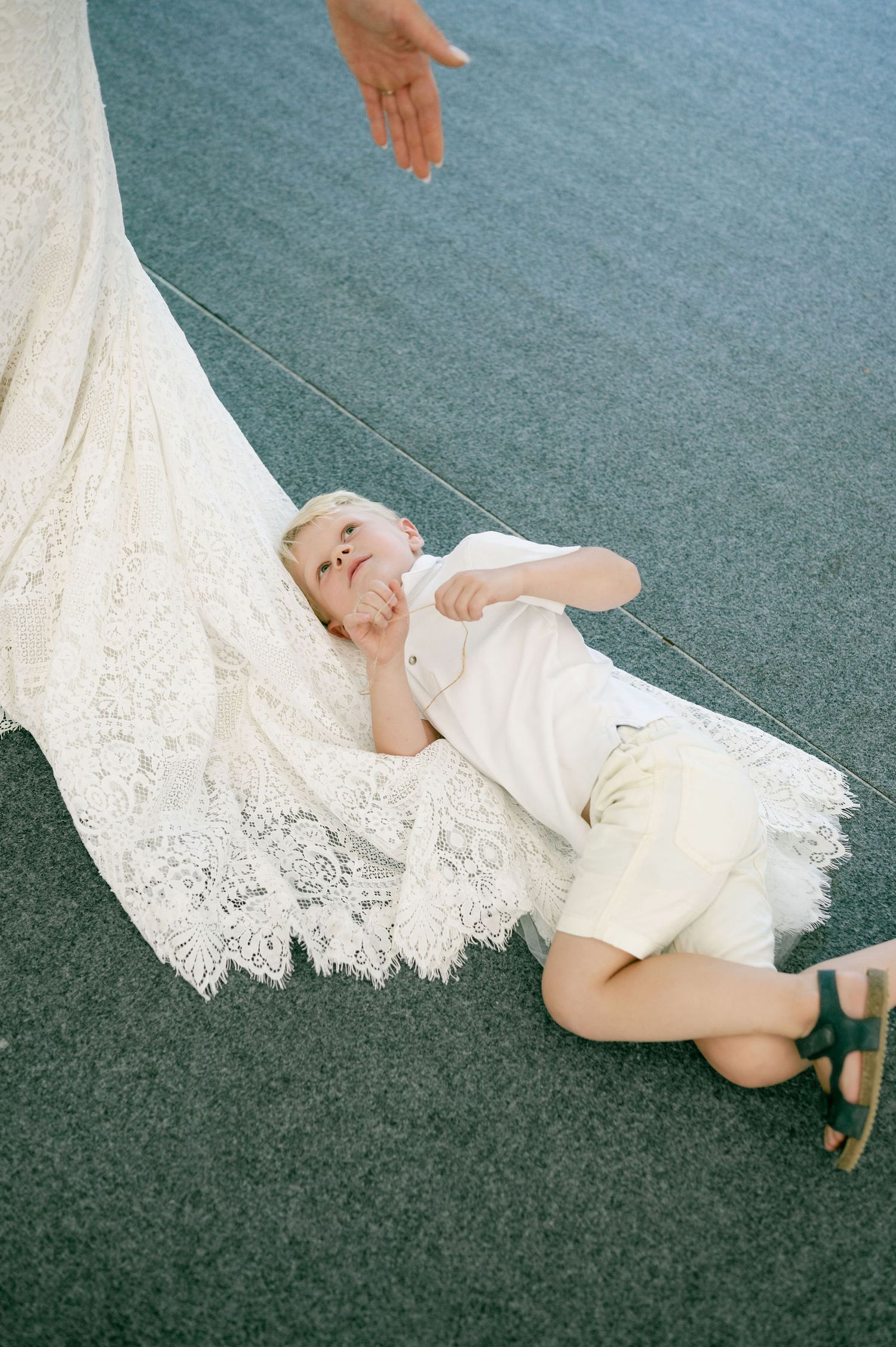 A person in white clothing lying on gray carpet with lace fabric draped nearby.