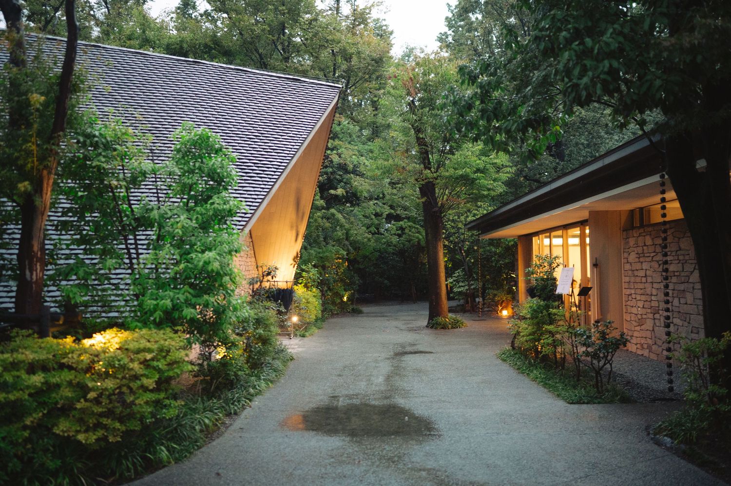 Stone lanterns illuminate a winding garden path leading to a rustic building entrance.