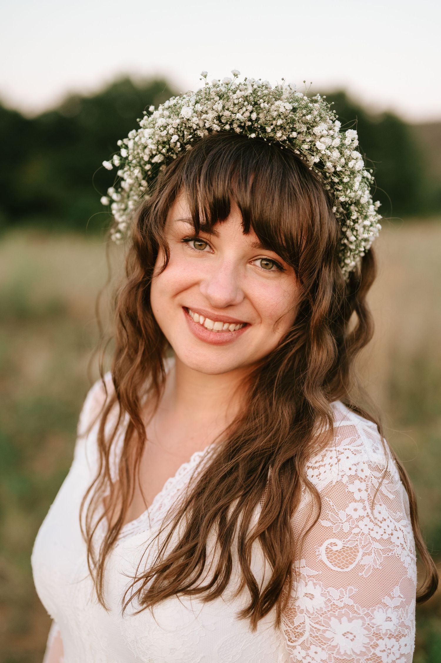 A bride wearing a lace dress and baby's breath crown smiles joyfully in natural light.