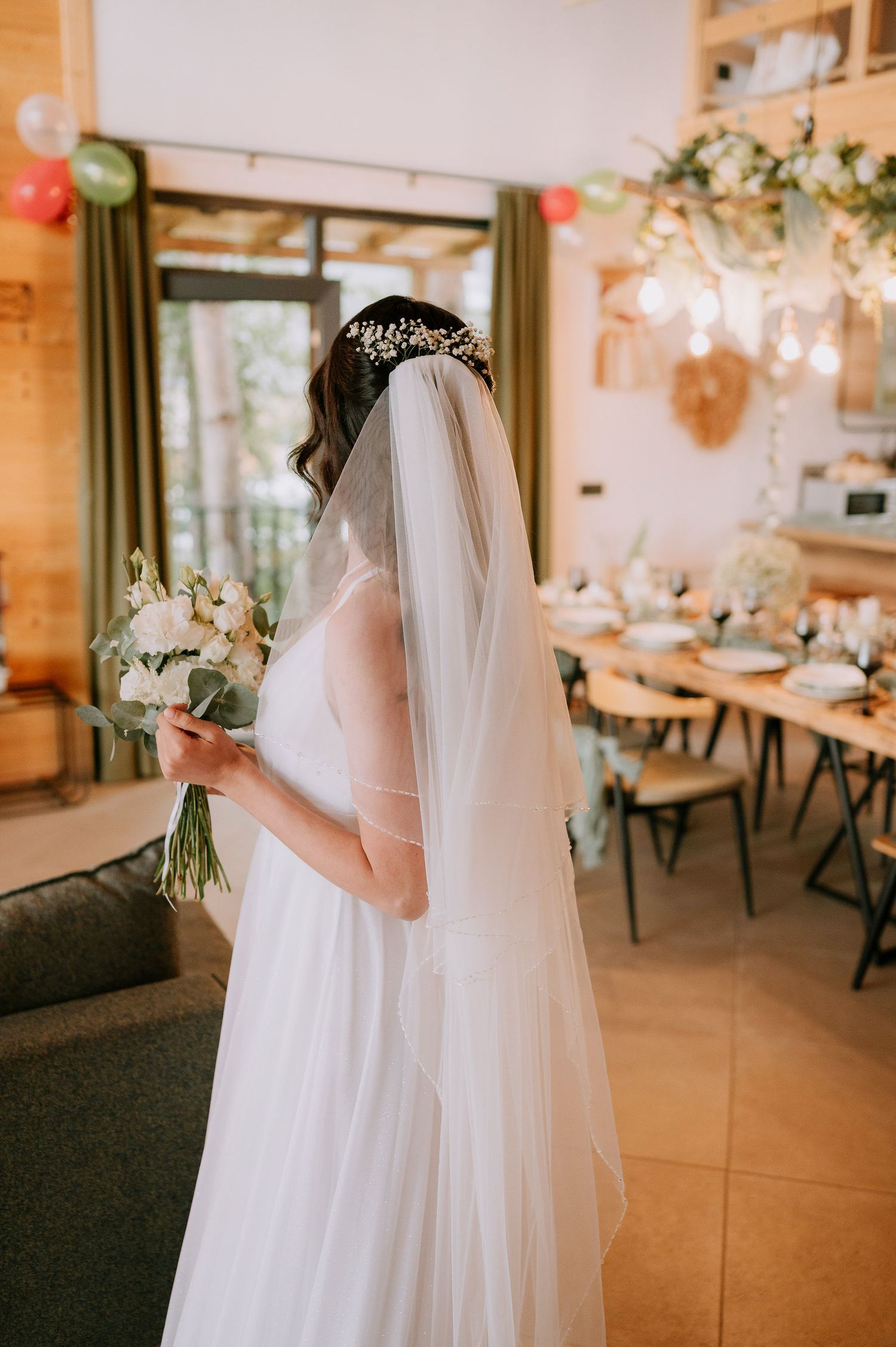 White-gowned figures stand in an elegantly decorated wedding venue with hanging lights and floral arrangements.