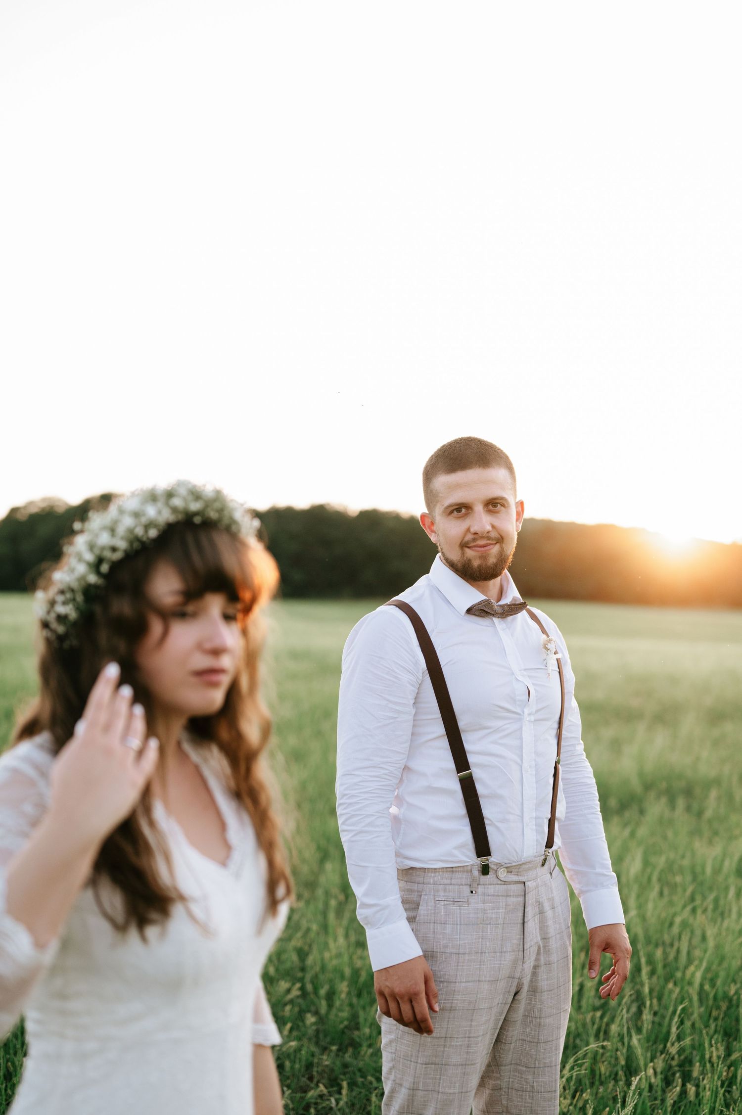 Golden hour wedding portraits in a field with bride in lace dress and groom in suspenders.