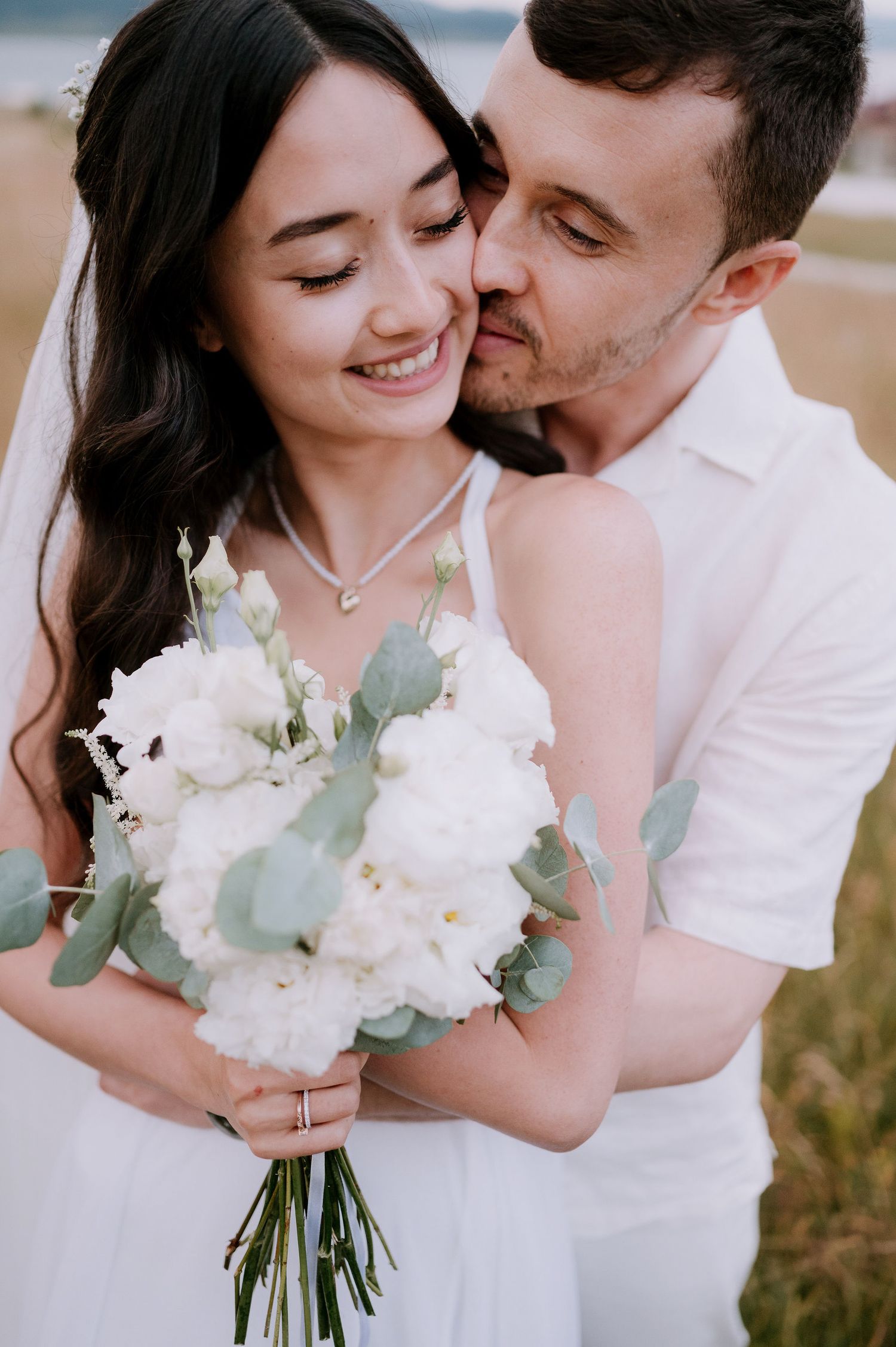 Intimate moment between couple with white bouquet against coastal landscape backdrop.