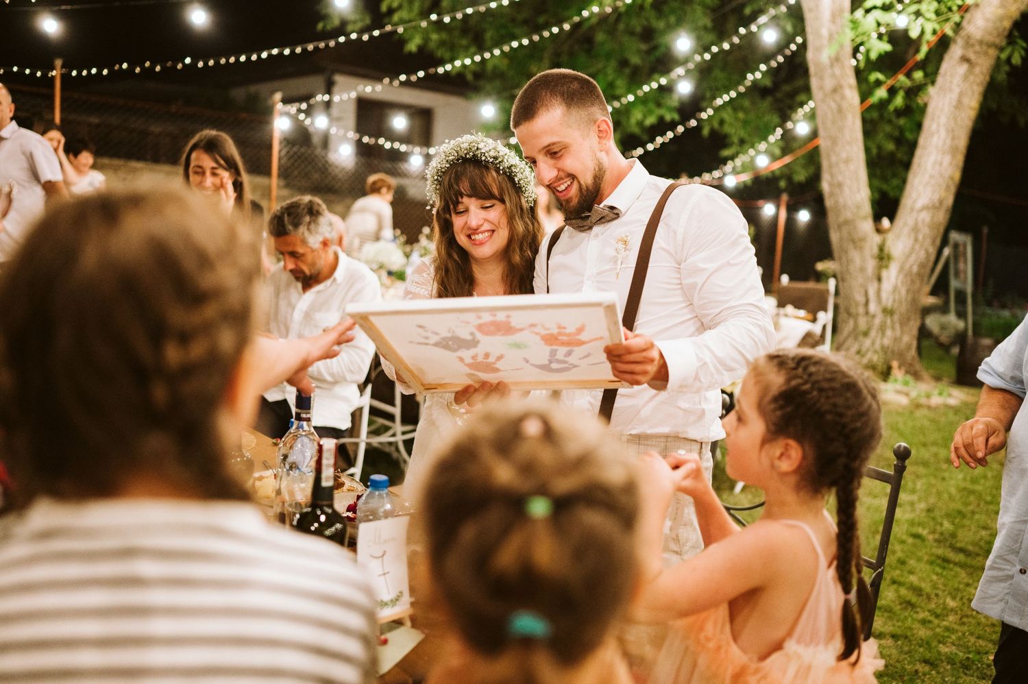 Wedding reception celebration under twinkling lights with guests gathered at tables.