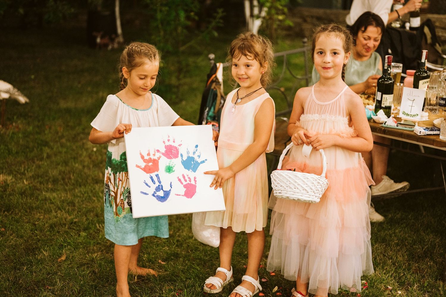 Young children displaying handprint art projects at an outdoor gathering.