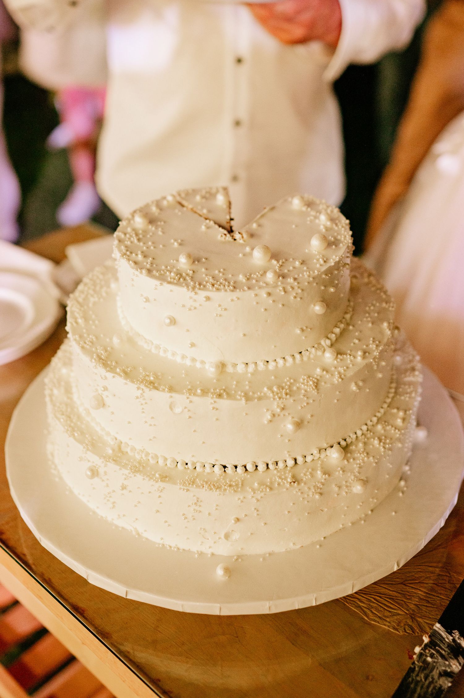 Elegant white wedding cake decorated with delicate pearls and intricate details on a wooden table.