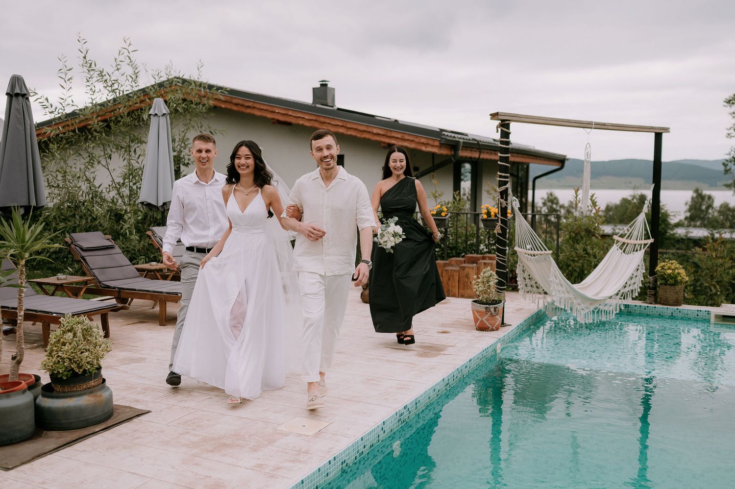 A poolside wedding celebration with guests in white attire gathered around a turquoise swimming pool.