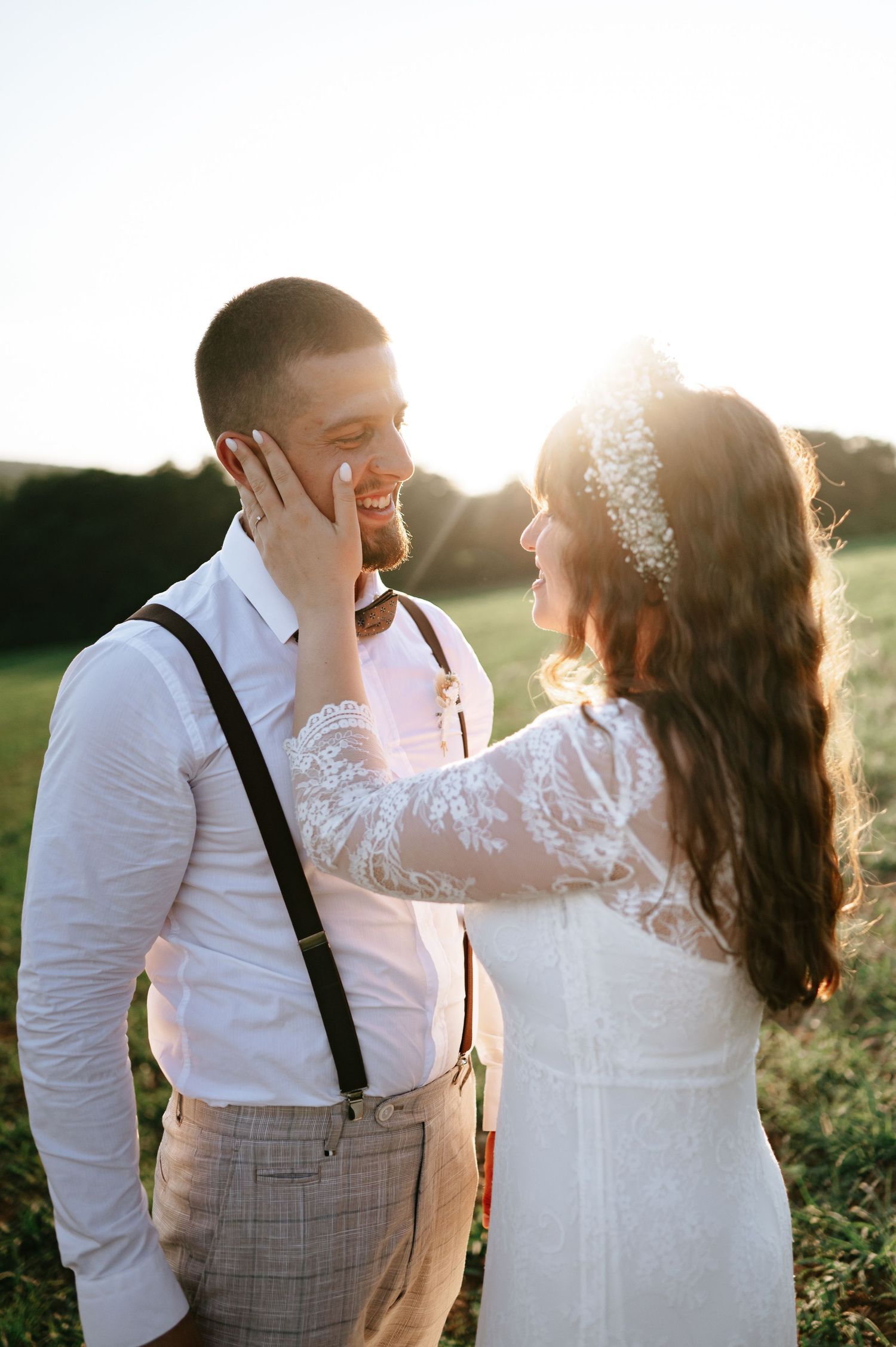 Newlyweds share an intimate moment in golden sunlight as bride touches groom's face tenderly.