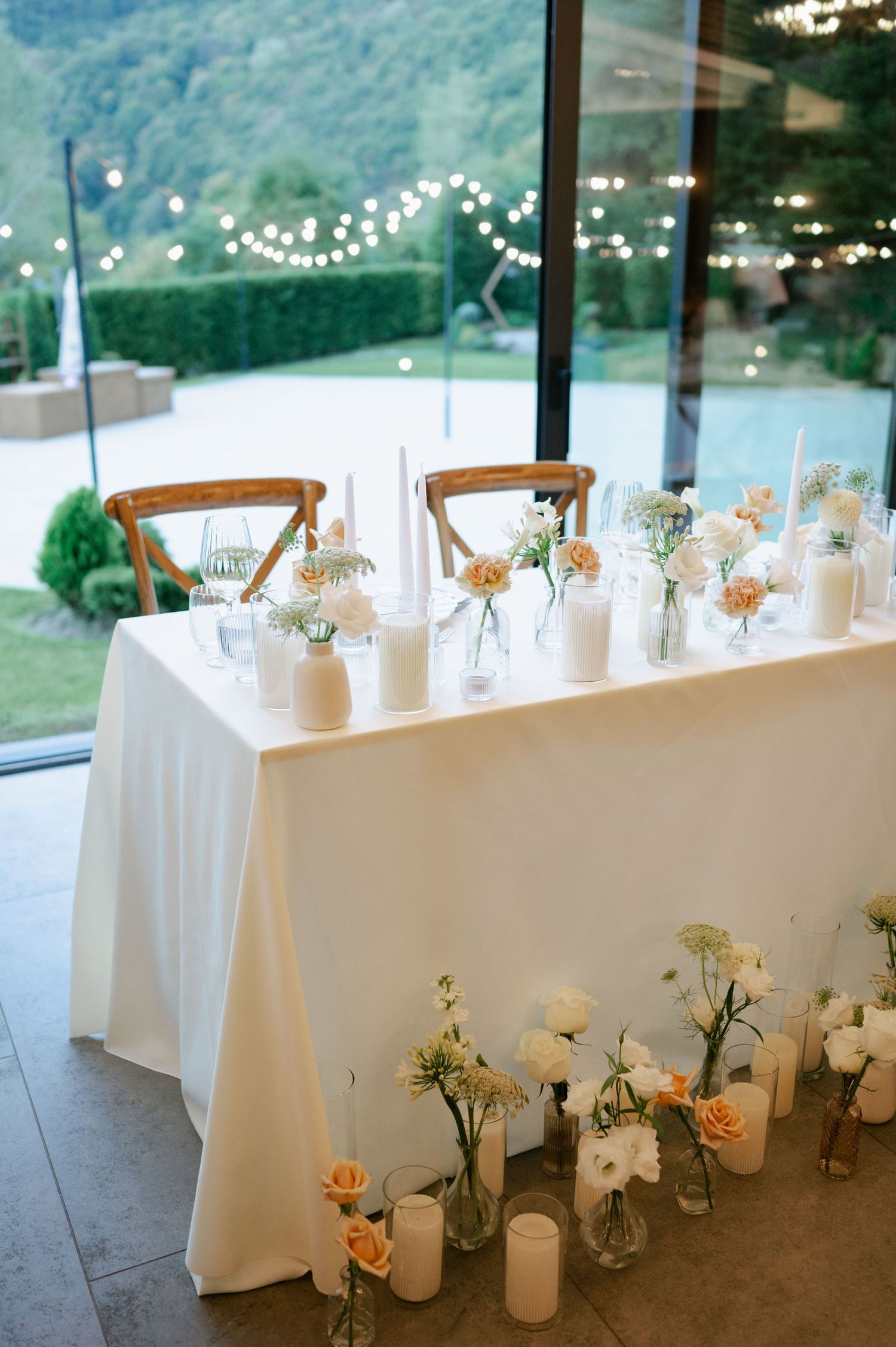 Elegant wedding table decor with white linens and small floral arrangements in glass vases against mountain views.