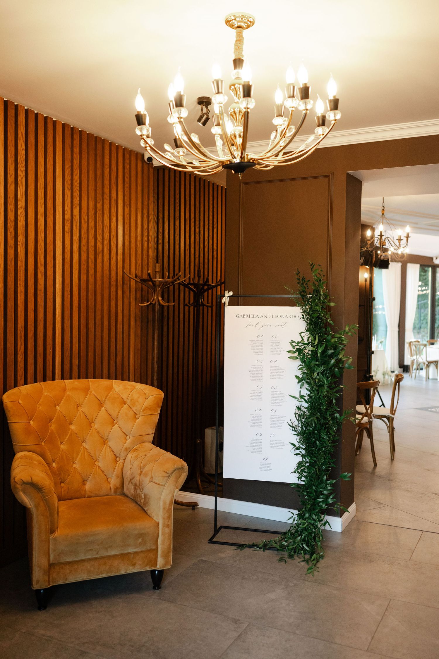 Luxurious lounge area with tufted velvet chairs and wooden accent wall panels under elegant chandeliers.