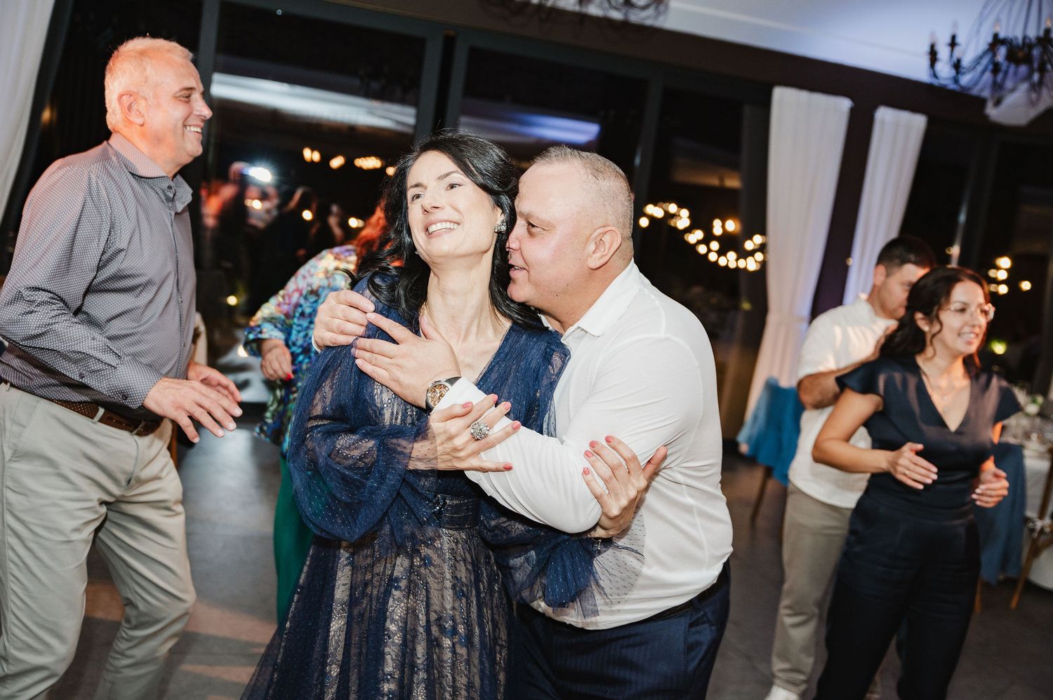 Wedding guests dancing and laughing together during evening reception celebrations.