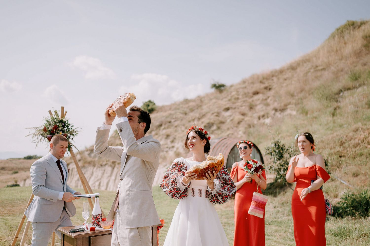Wedding party celebrates outdoors with bridesmaids in coral dresses against a hillside backdrop.