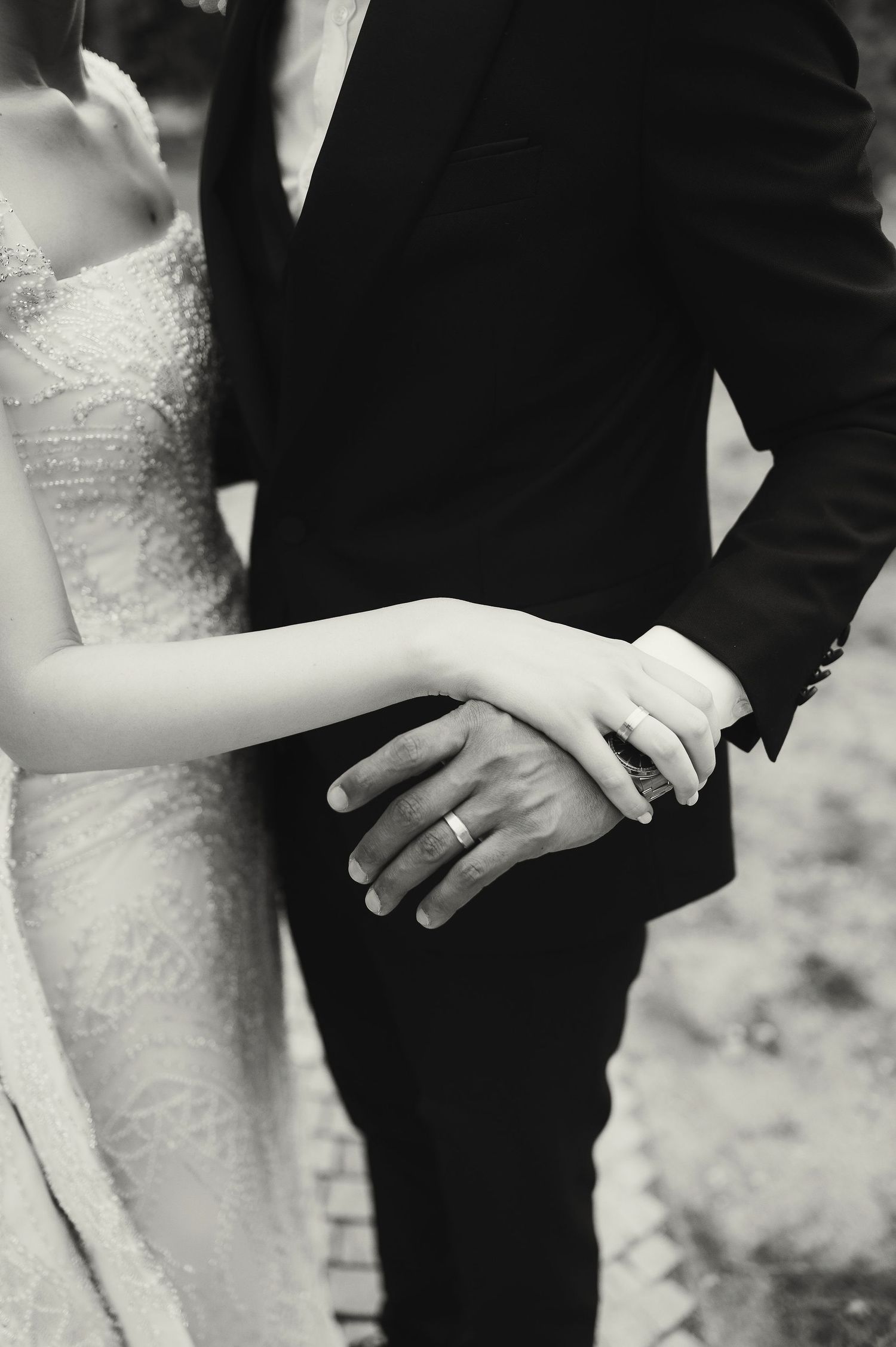 A black and white detail shot of formal wedding attire and hands.