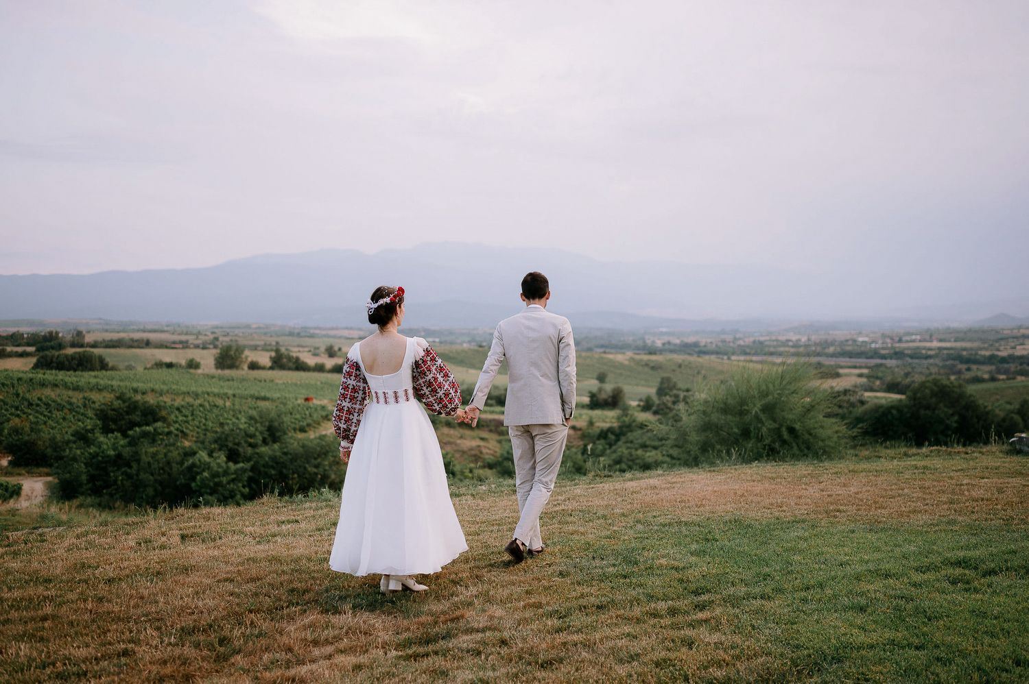 Wedding couple holding hands while walking through scenic mountain meadow.