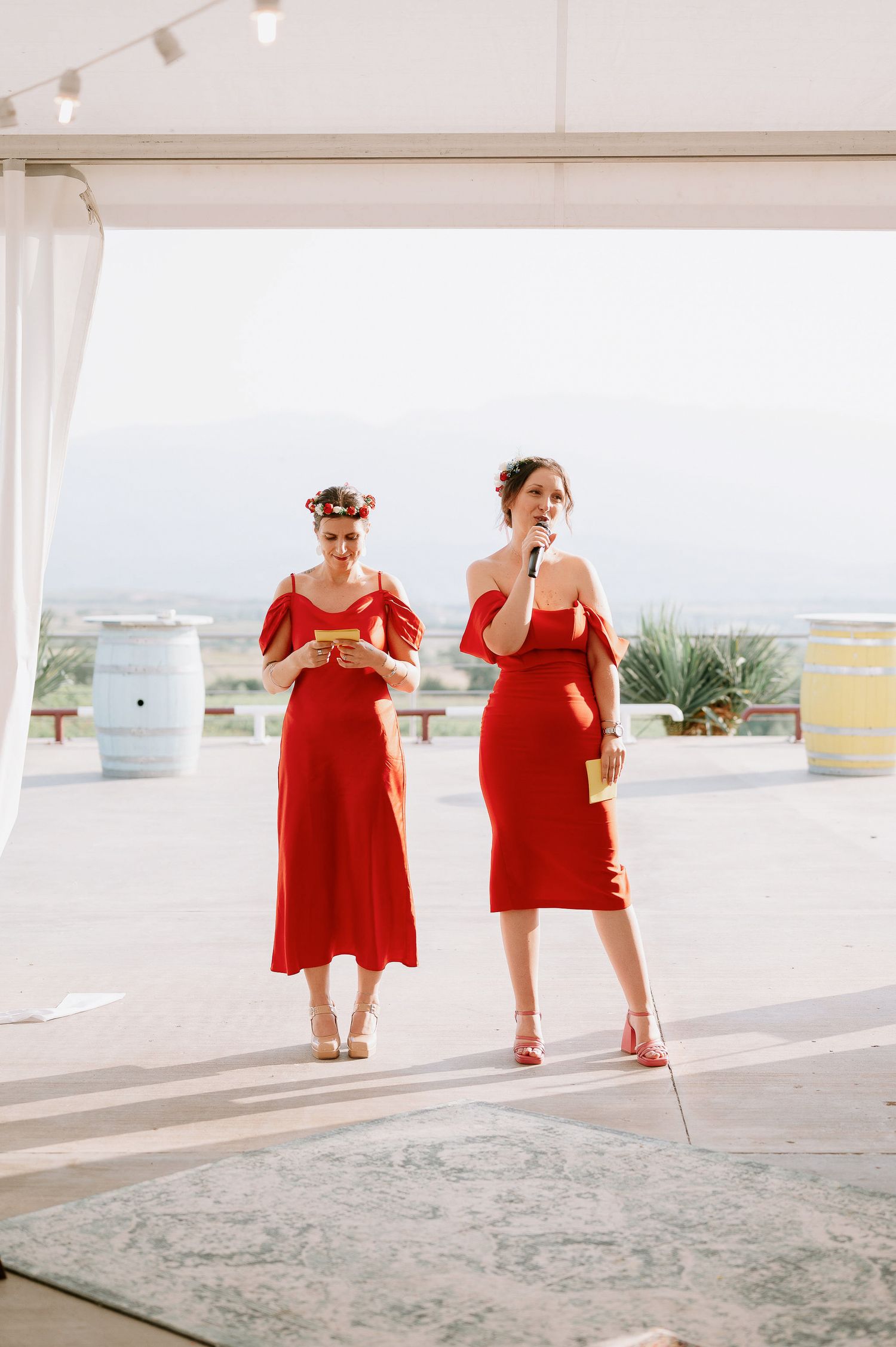 People in red attire walk along a bright coastal terrace with white railings.