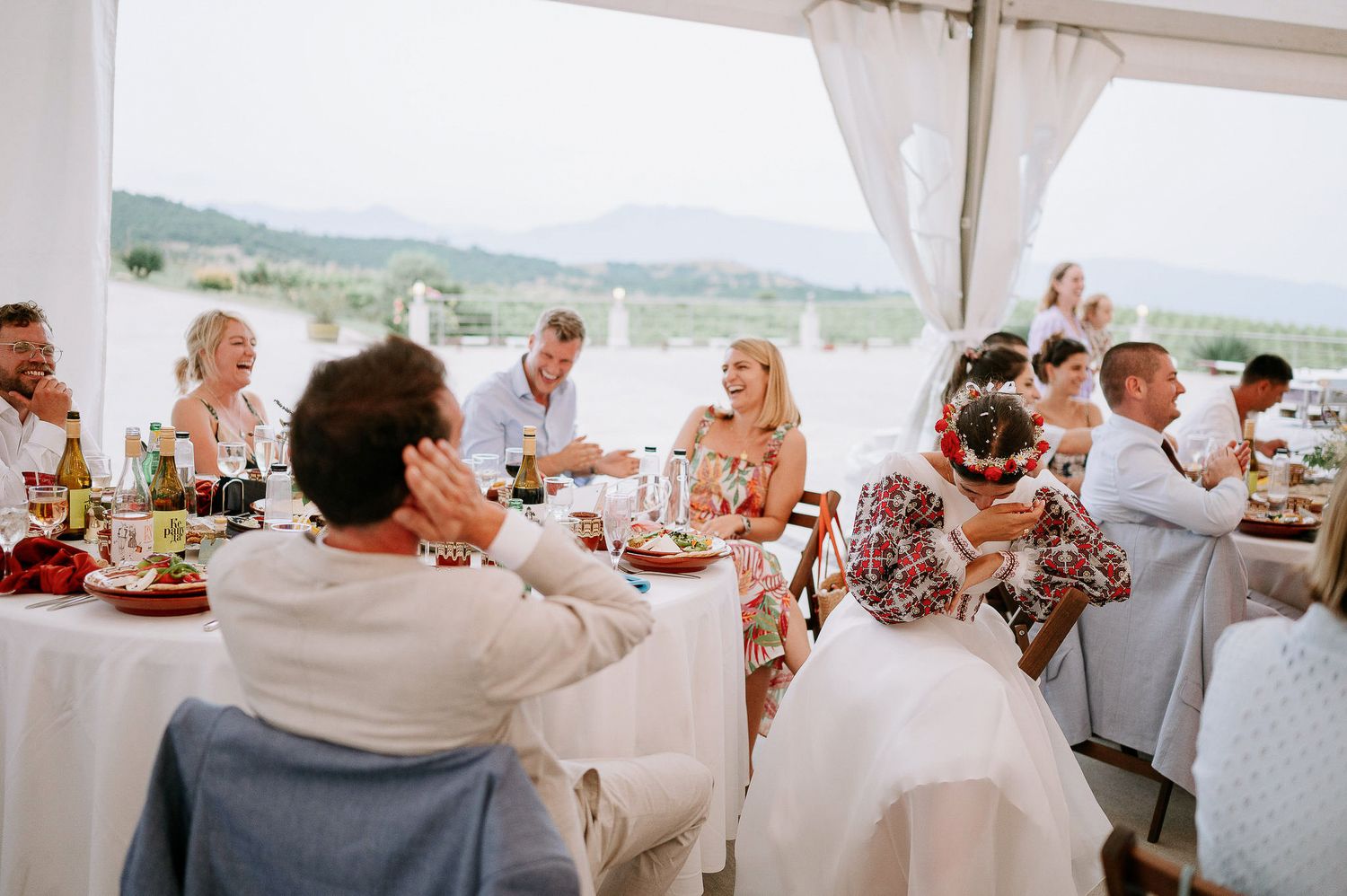 Wedding reception guests seated at tables under a white tent pavilion overlooking scenic mountains.