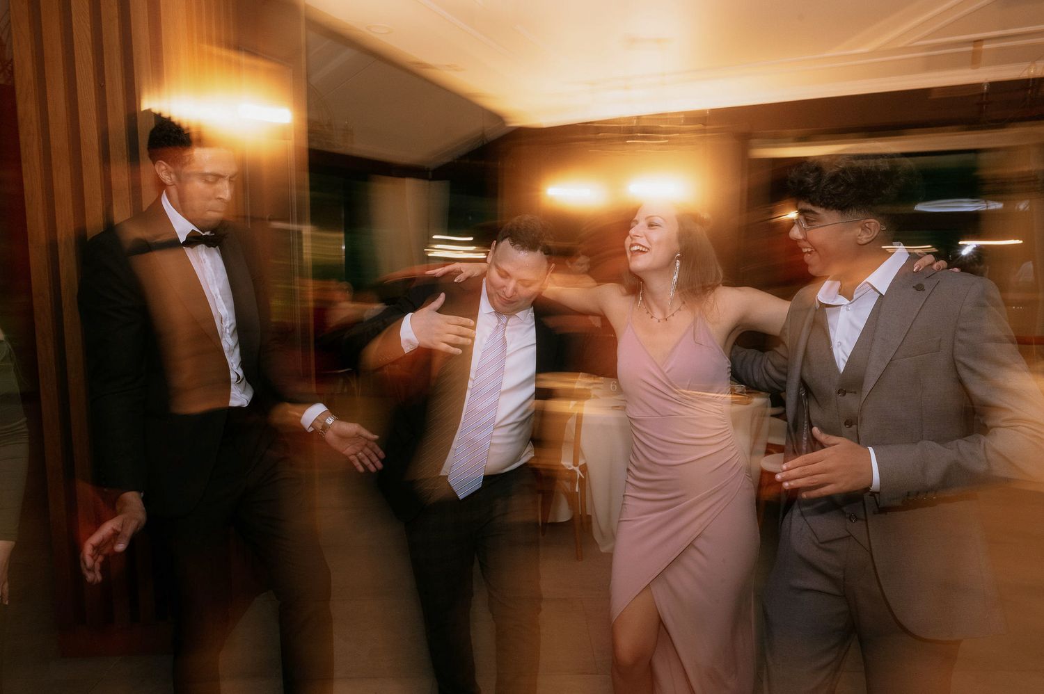 Blurred candid shot of wedding guests dancing and laughing at reception.