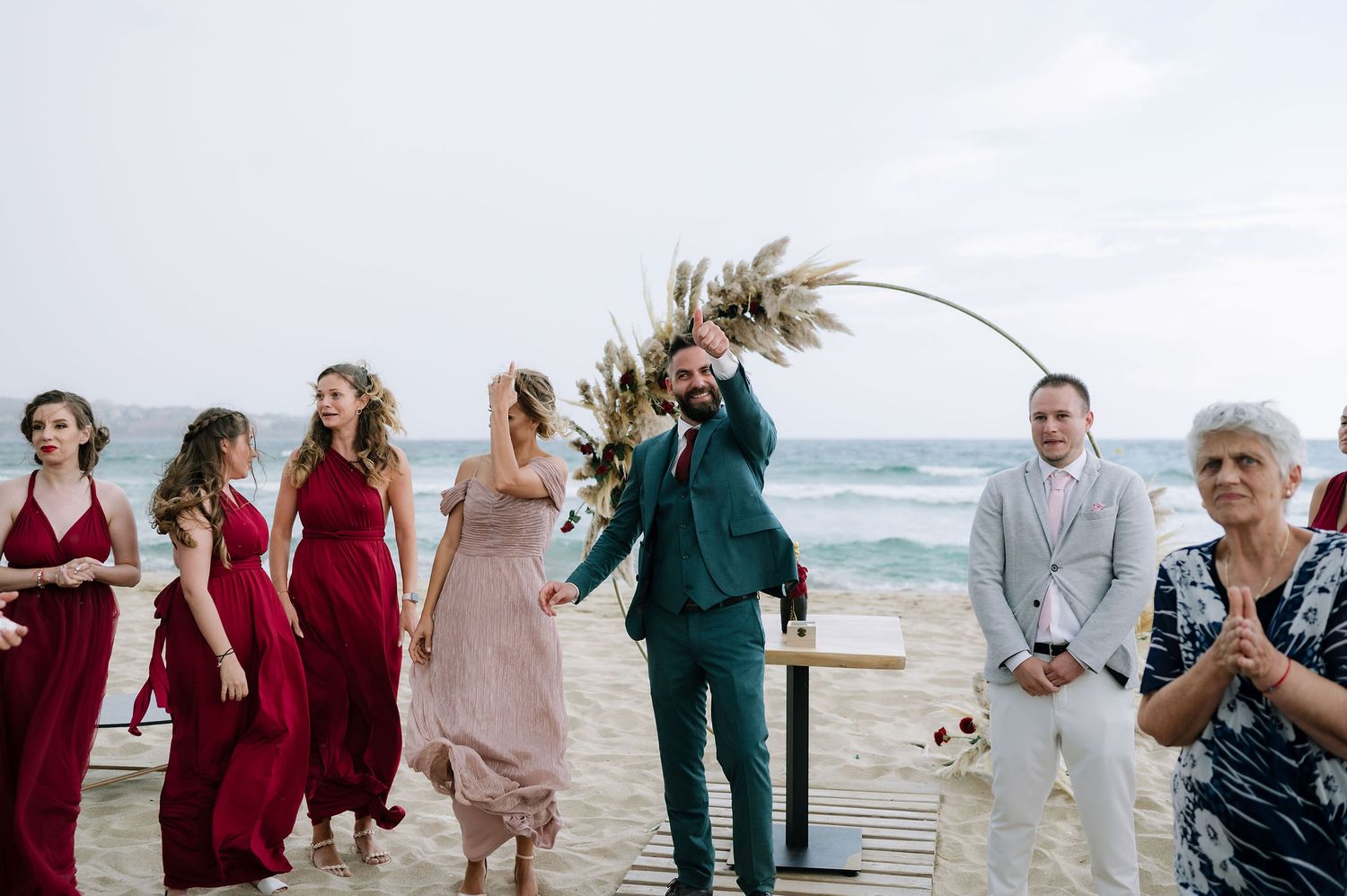 Wedding party and guests celebrate on a beach boardwalk with the ocean in the background.