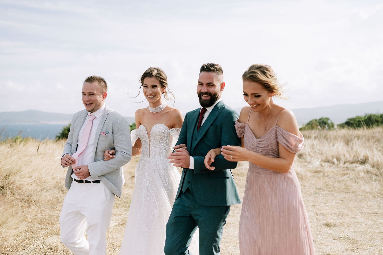 Wedding party walking together through tall grass in natural lighting.