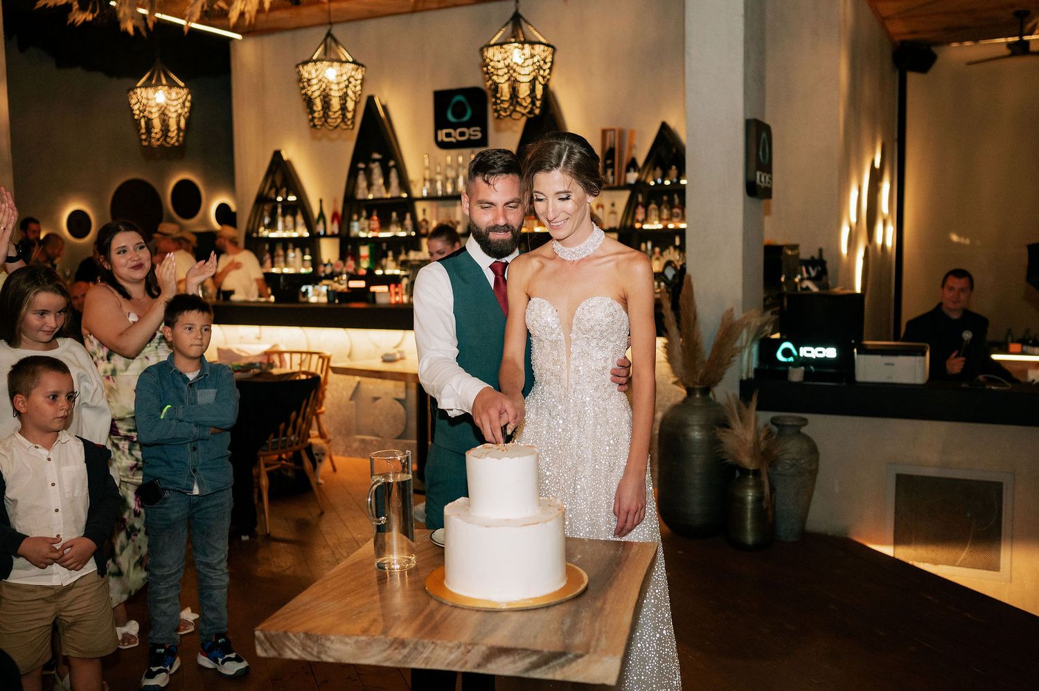 Wedding reception venue decorated with lanterns and guests gathered around white cake.