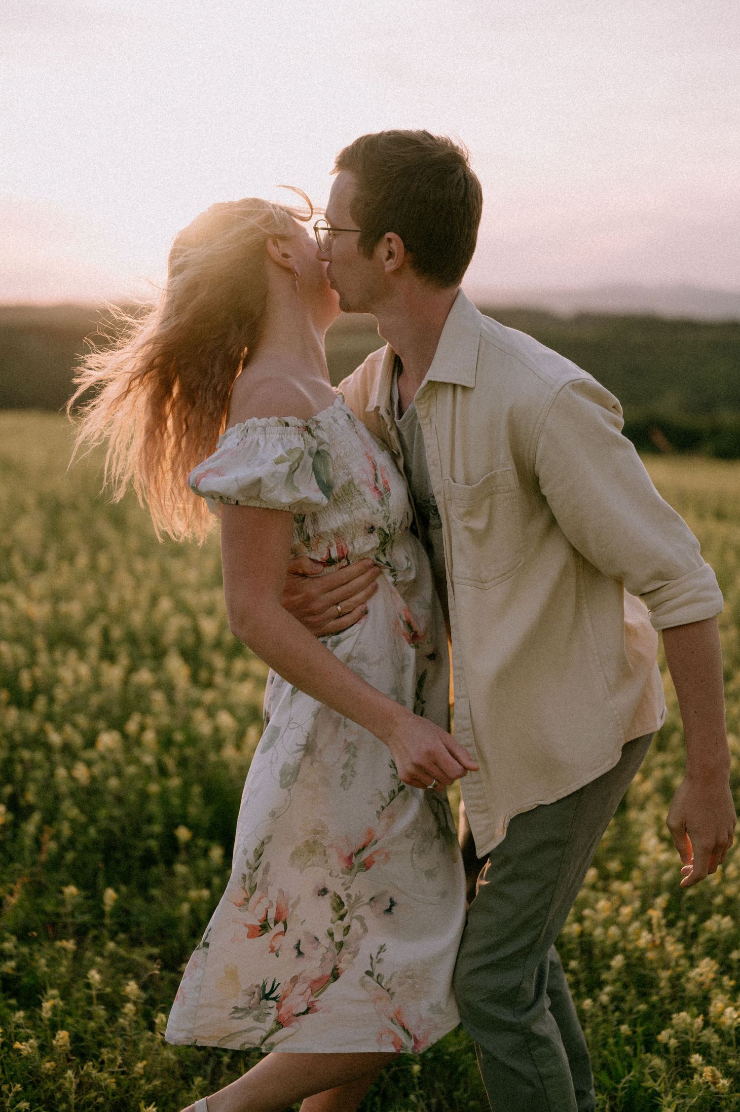 Romantic couple sharing an intimate moment in a blooming yellow flower field at sunset.